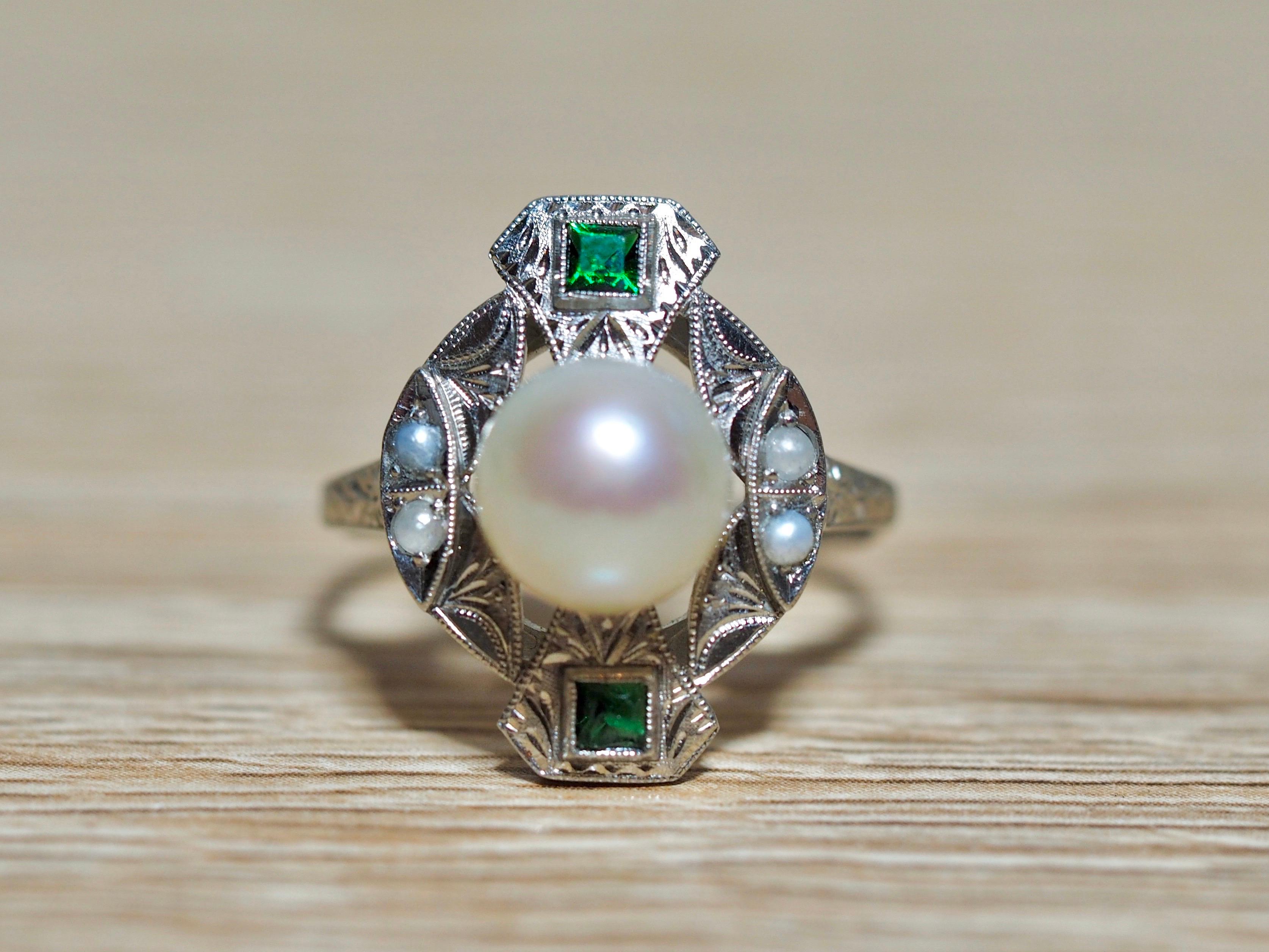 This sophisticated Edwardian platinum ring is incredible. The center features an 8.60 MM natural pearl. There are two accenting green squared emeralds with four smaller natural pearls on the sides. Beautiful scroll work is flowing throughout the