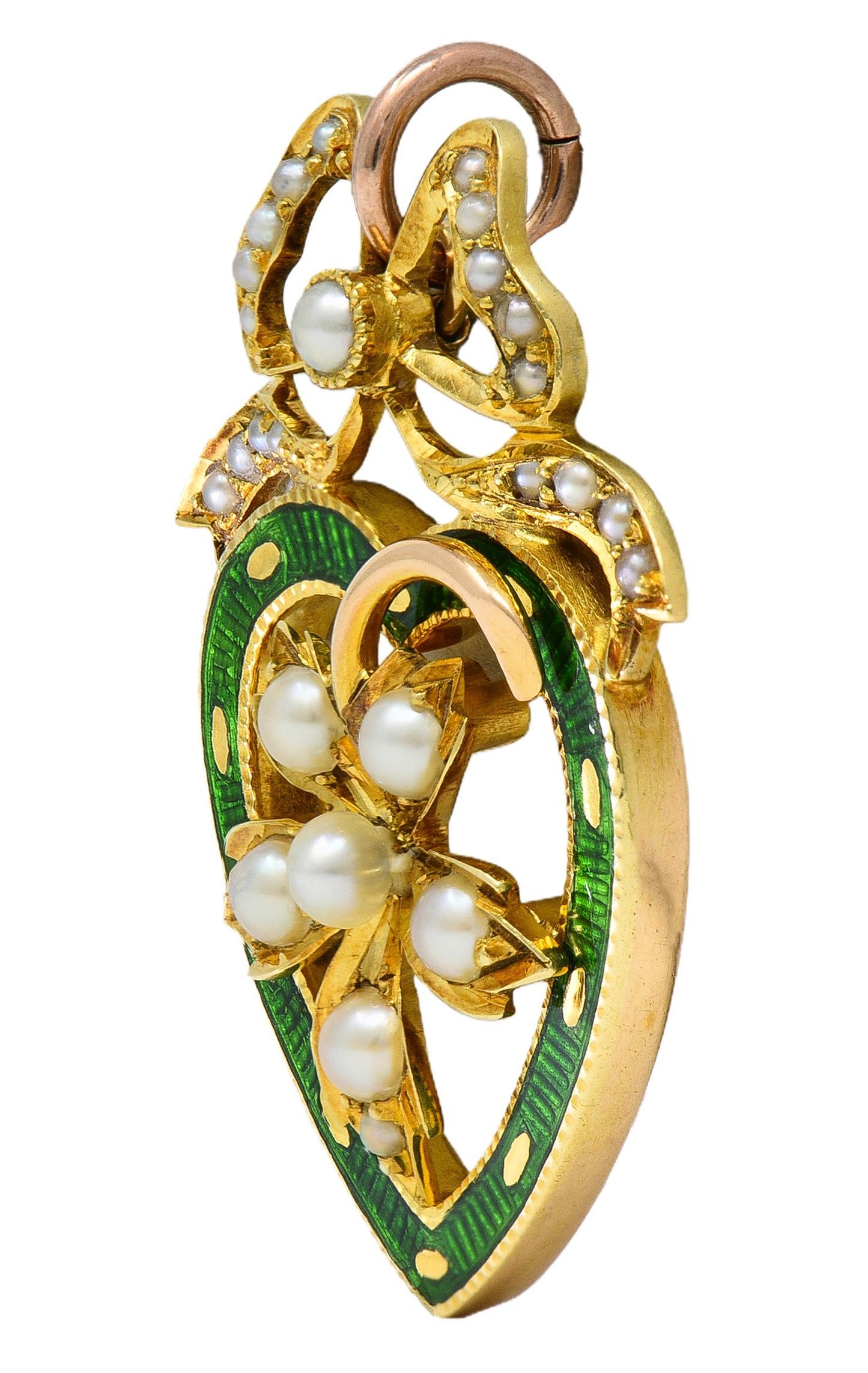 Designed as a heart shaped form topped with bow motif and centering a stemmed flower
Heart is glossed with transparent green bassé-taille enamel over linear engraving
Bow and flower are bead and bezel set with seed pearls throughout
Measuring 1.0 to