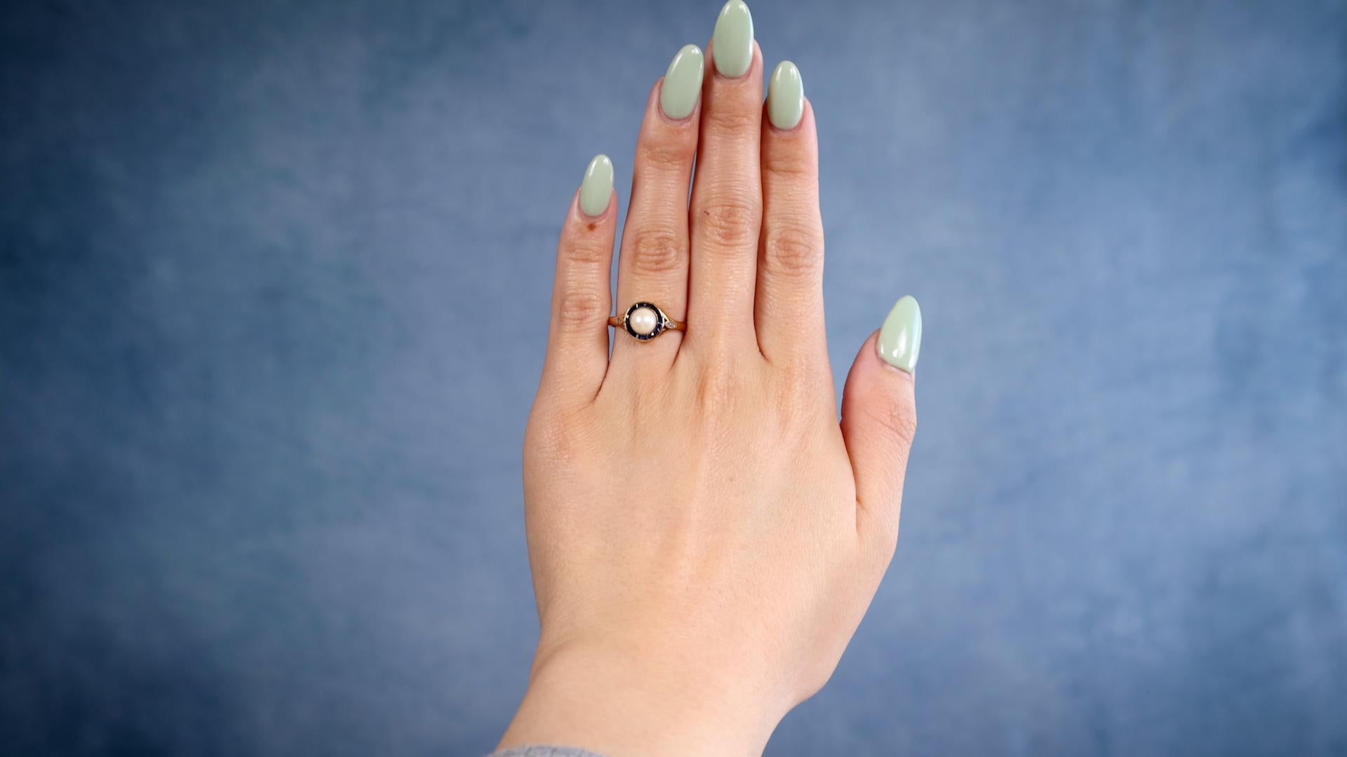 Ein Edwardian Perle Saphir Diamant 18k Gelbgold Platin Ring. Mit einer cremefarbenen Perle von etwa 5,75 Millimetern. Akzentuiert durch 16 Saphire im Kaliberschliff mit einem Gesamtgewicht von ca. 0,35 Karat und zwei Diamanten im Senaille-Schliff