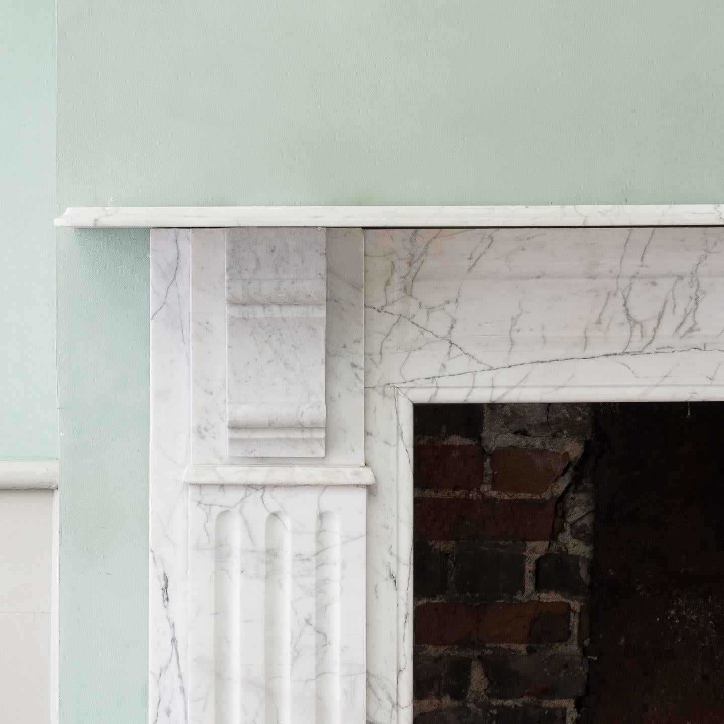 An Edwardian pencil vein marble chimneypiece, the thumb-moulded shelf above panelled frieze flanked by plain corbels, the stop-fluted marble jambs on square foot blocks. In good clean condition. In good clean condition, the shelf with slight bow.