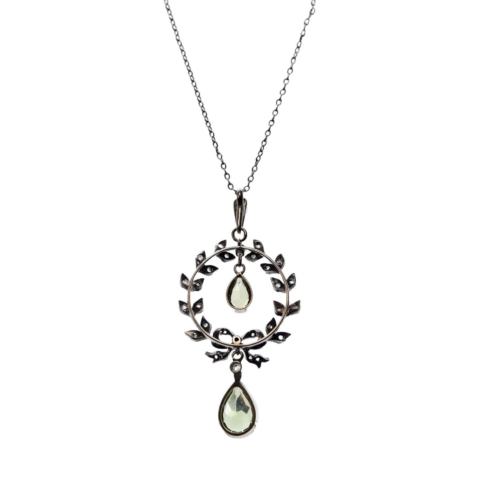 An Edwardian period peridot, diamond, and pearl pendant in platinum and 18 karat yellow gold. Designed as a diamond set platinum wreath, this pendant is centered by two pear shaped peridot's. Set in 18 karat yellow gold bezels complete with