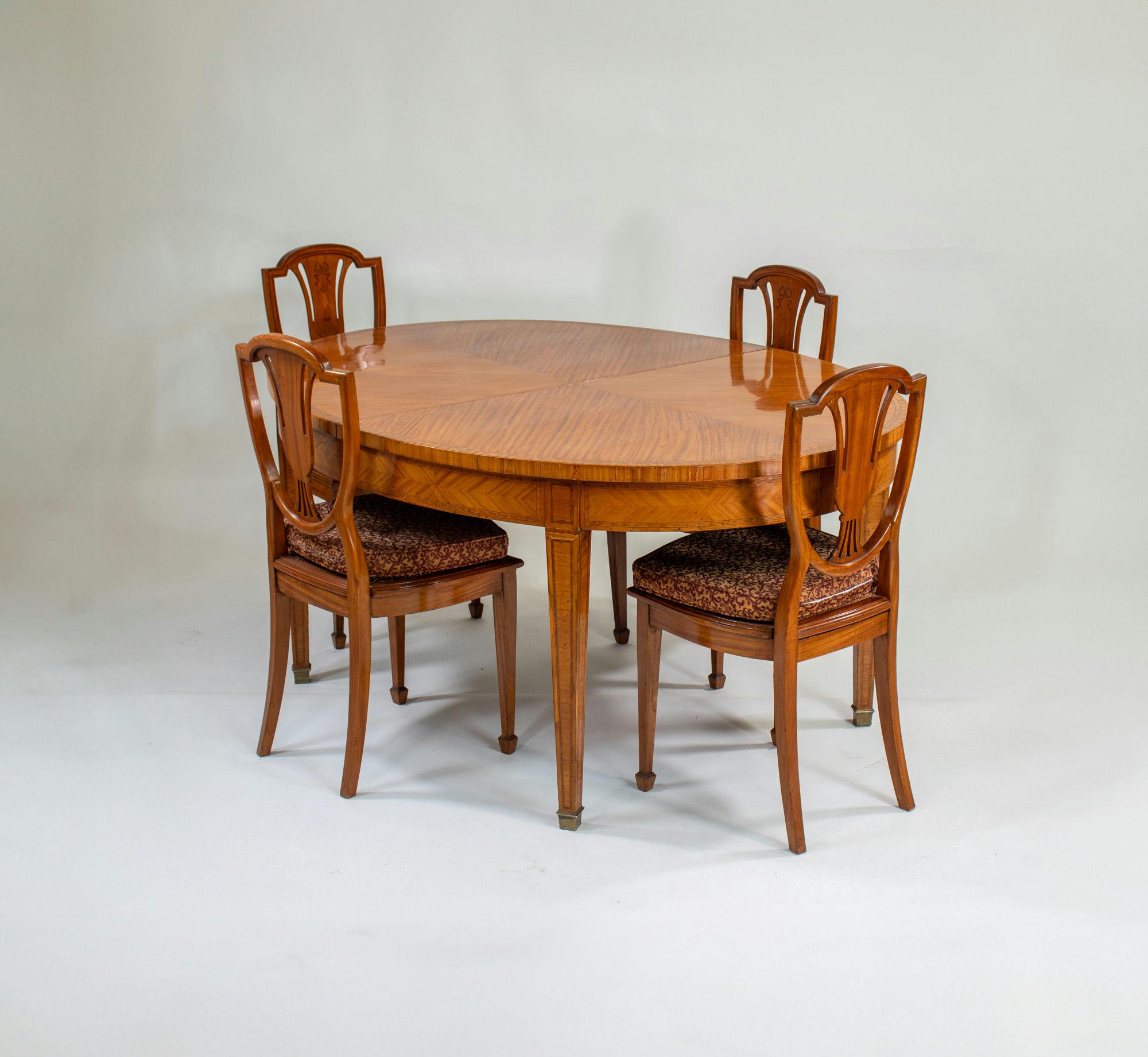 Cet ensemble de salle à manger en bois satiné de style édouardien anglais s'inspire du travail de George Hepplewhite. L'ensemble est composé d'une table ovale et de huit chaises à dossier bouclier. La table est dotée d'une feuille amovible, ce qui