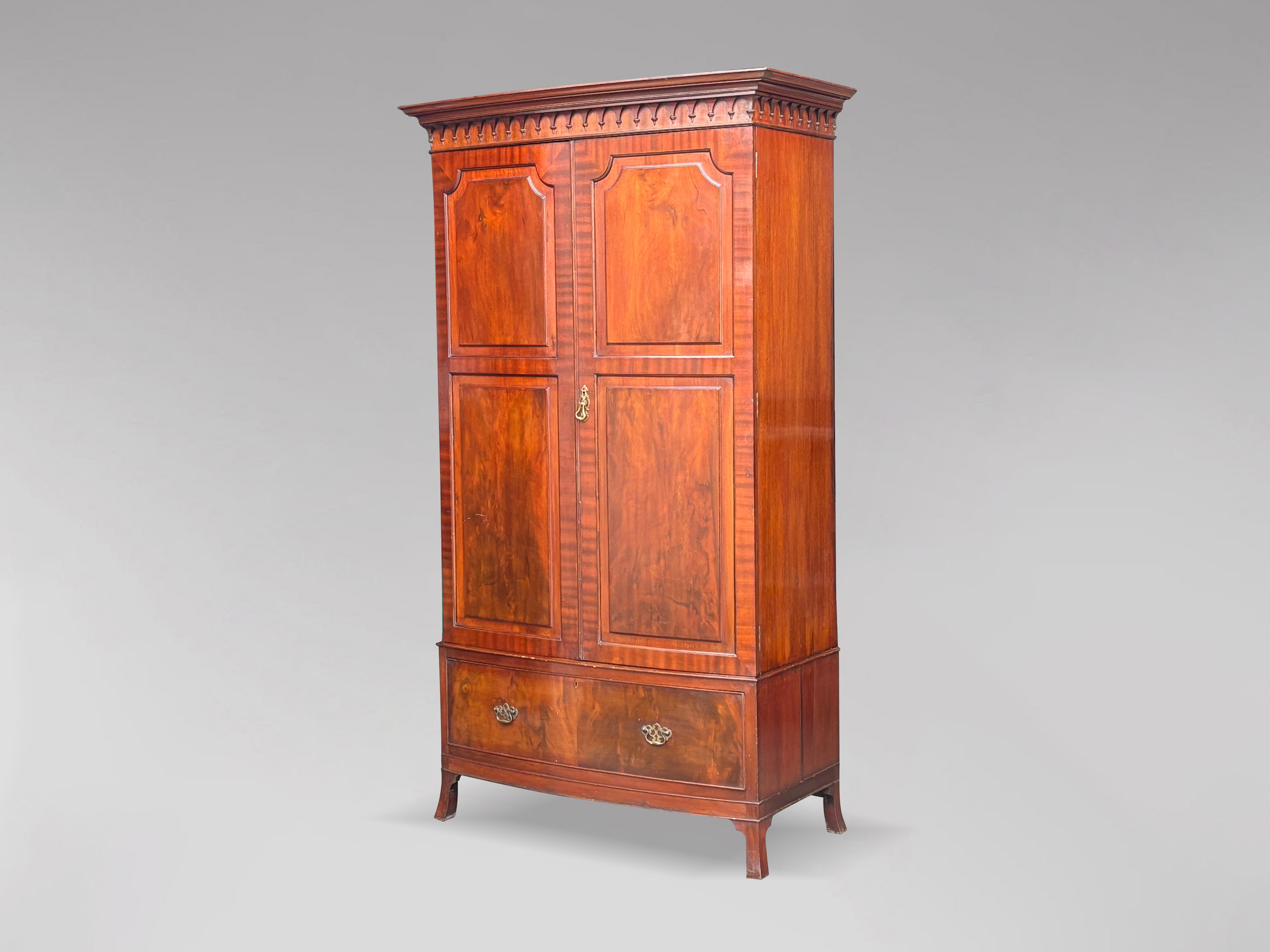 An early 20th century, Edwardian period mahogany bow front 2 door wardrobe. The stepped moulded cornice above a deep frieze with carved arched finials, above two tall bow fronted doors with moulded panels opening to reveal a pair of steel pull out