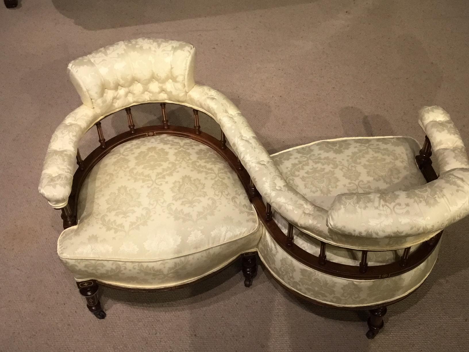 An Edwardian period mahogany inlaid antique love seat. Having an S shaped mahogany frame incorporating two sprung seats with deep buttoned padded supports and arms, with turned and inlaid spindle supports. Raised on six turned mahogany supports with