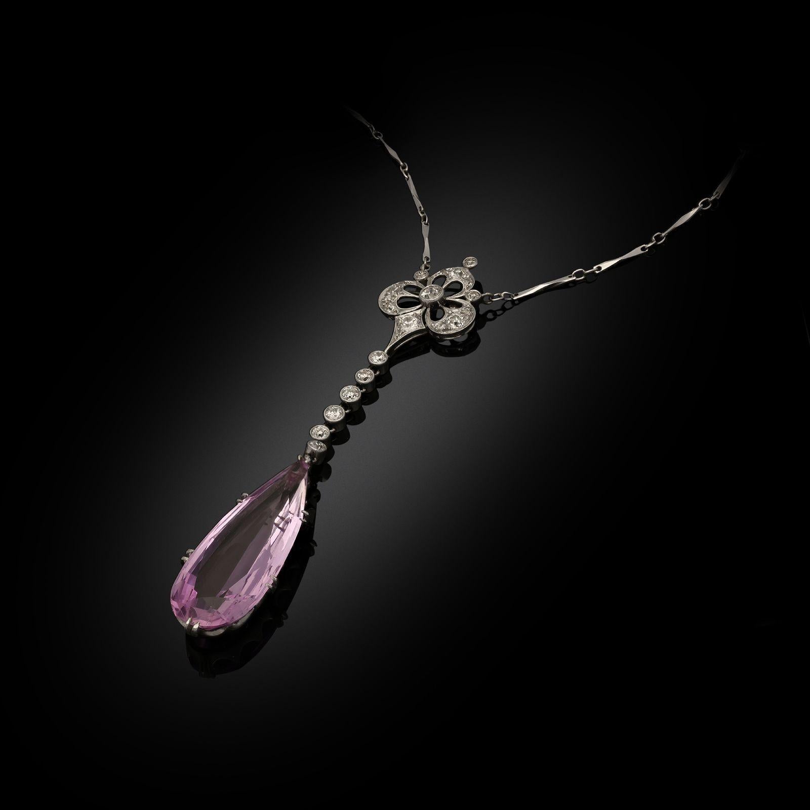 An elegant Edwardian topaz and diamond pendant c.1910, set with a beautiful elongated pear shaped pink topaz drop in minimal platinum claw setting suspended beneath a run of six old European cut diamonds in rub over settings beneath an openwork