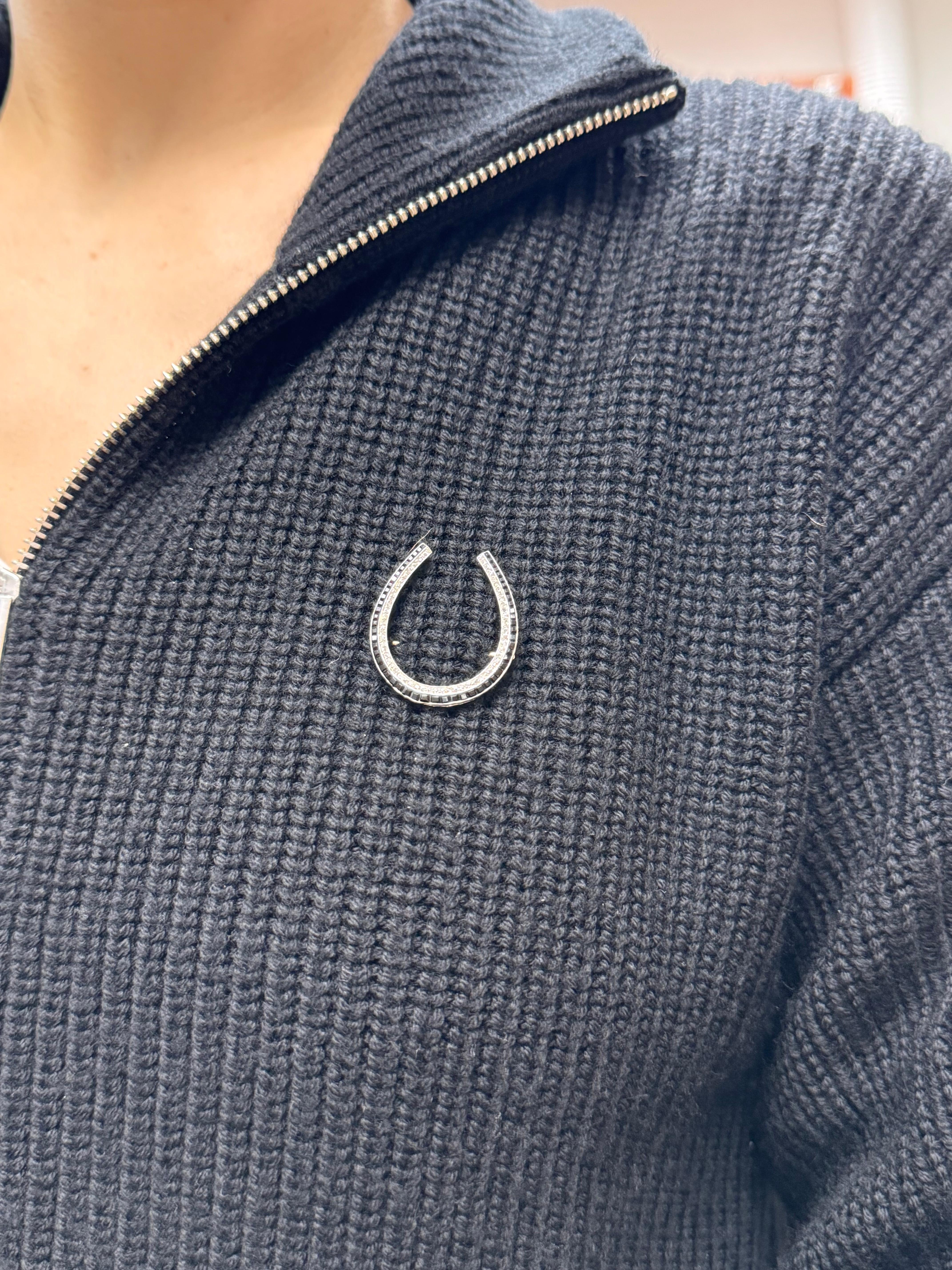 This Edwardian era horseshoe pin features French cut onyx and single cut diamonds set in platinum. Weighing 5.8 grams, the design showcases a symmetrical horseshoe shape, measuring approximately 1 1/8 inches in both length and width. The inner row