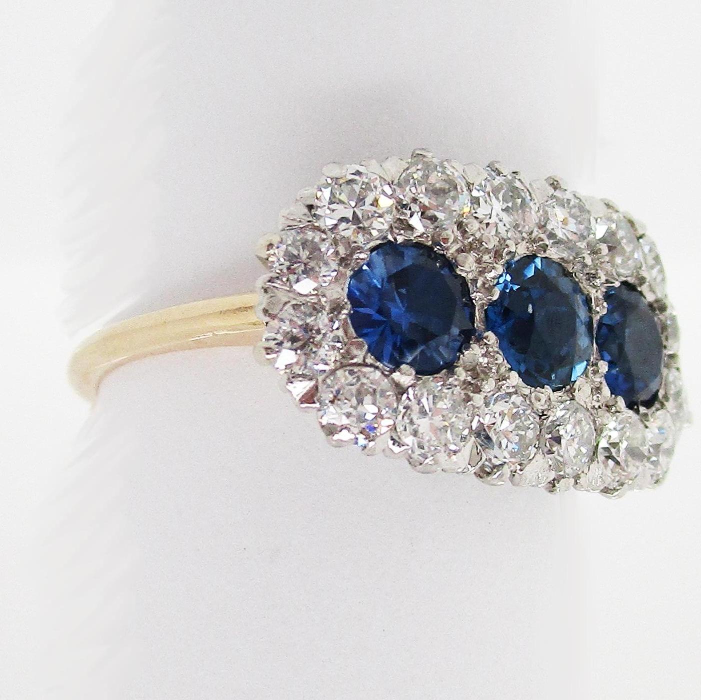 This is an absolutely breathtaking Edwardian ring in platinum and 14k yellow gold, featuring three stunning sapphires framed by a row of white old mine cut diamonds. This ring has a stunning unique layout and a gorgeous overall look! The ring has a
