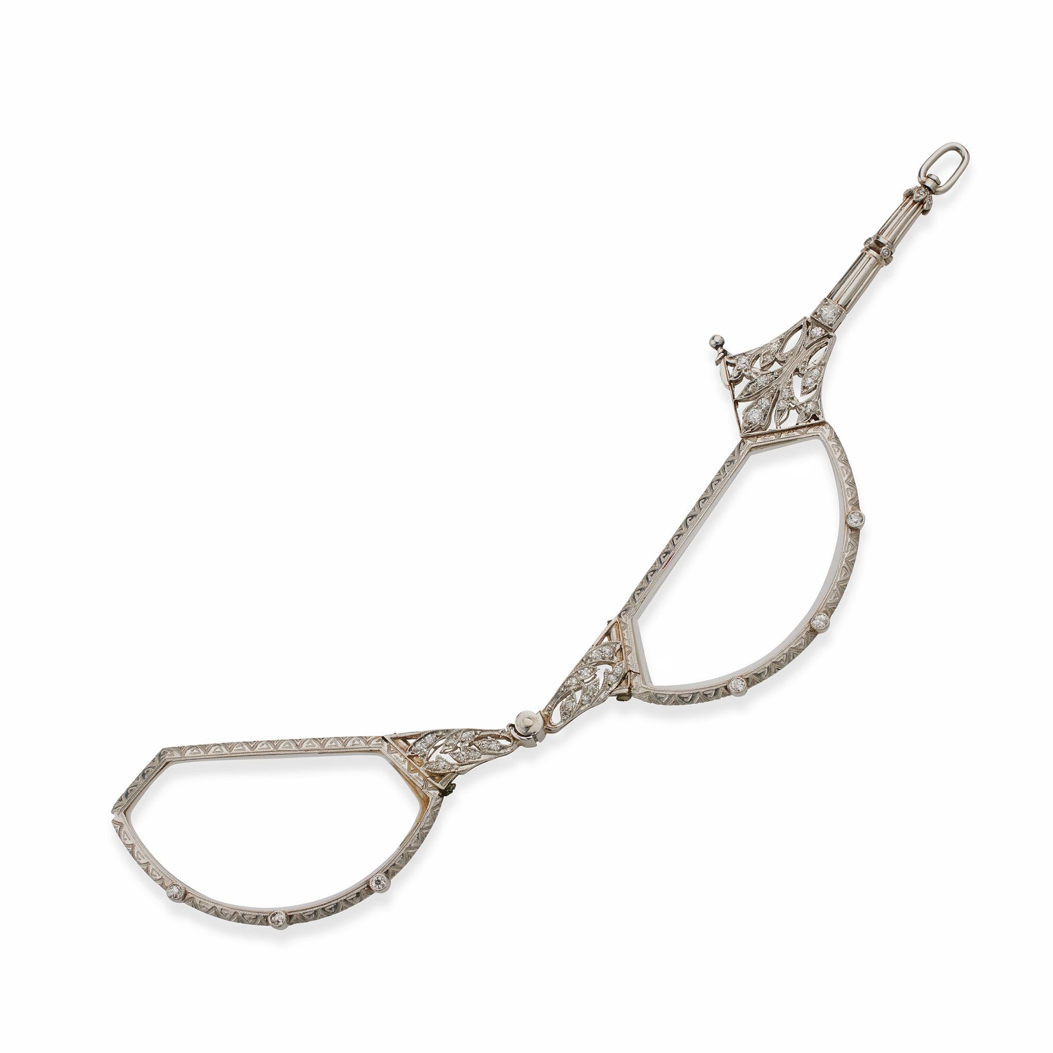 Risalente al 1900-1910 circa, questo pendente lorgnette edoardiano è composto da platino e diamanti. La lorgnette è formata da una colonna con elementi foliati di diamanti traforati che sospendono lenti da lettura retrattili con cornici a motivi