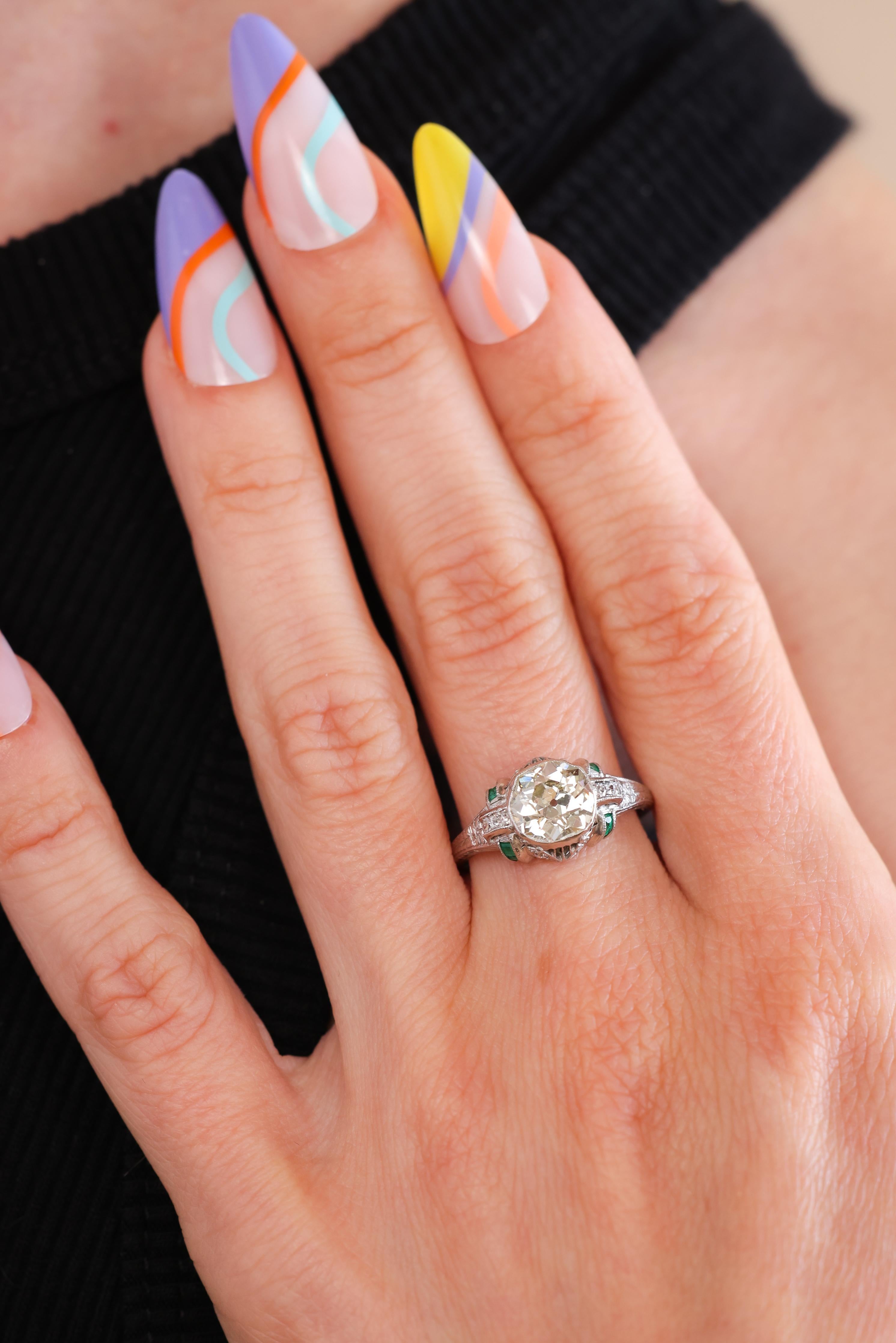 This is a gorgeous and authentic Antique Edwardian era (circa 1920) platinum engagement ring. The ring centers a bezel set diamond accompanied by a GIA Diamond Report stating the 1.85ct Old Mine Brilliant Cut stone is graded M color and SI1 clarity.