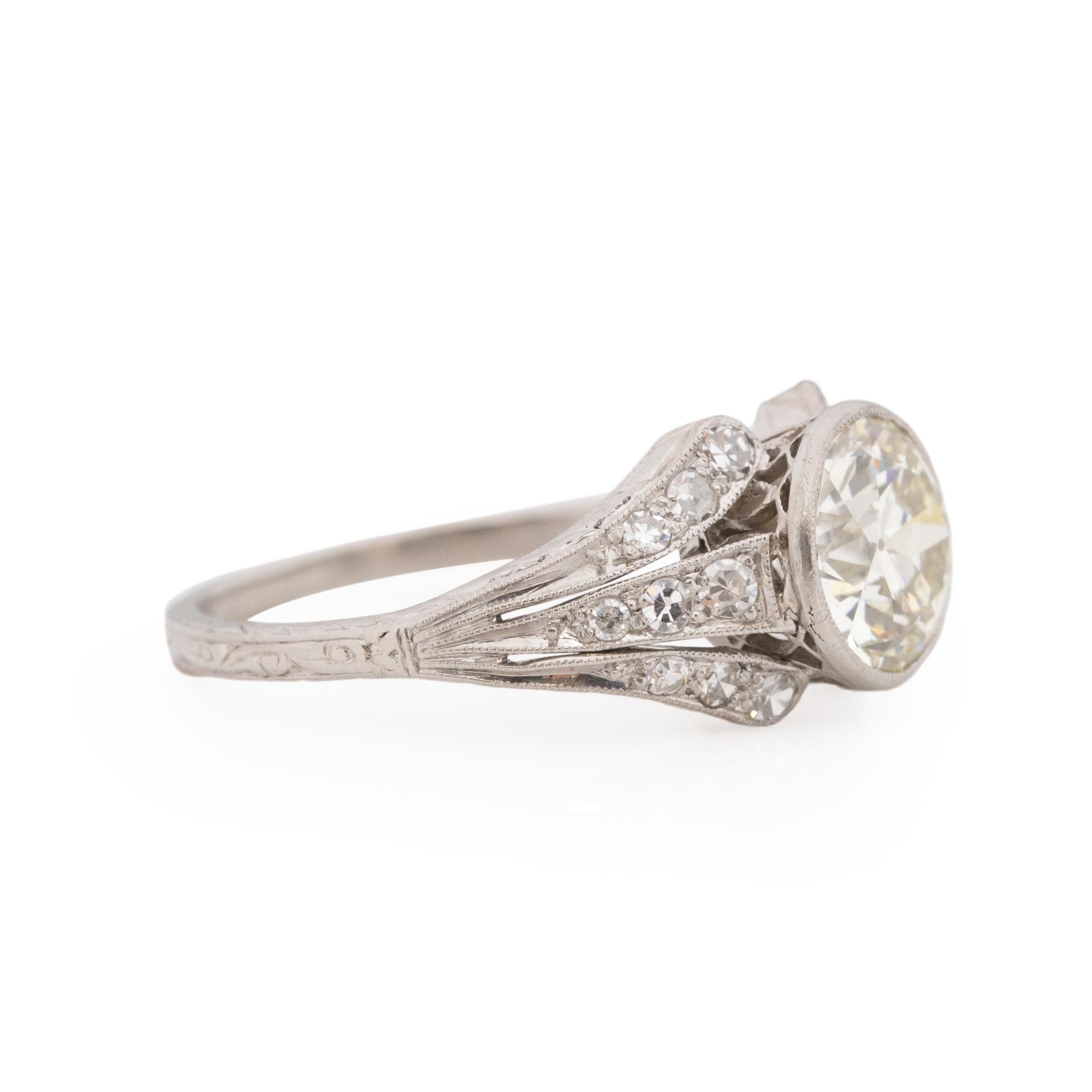 Here we have a perfectly hand-crafted platinum Edwardian era engagement ring. Starting at the shanks, which is engraved with a leaf like repeating pattern that almost wraps completely around the ring. The little bit of wear that shows is the