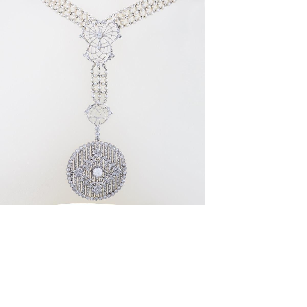 An Edwardian platinum sautoir necklace with diamonds and seed pearls. The necklace is comprised of a chain with five rows of seed pearls, interspersed with complex decorative filigree work and studded with diamonds. It has a hanging pendant