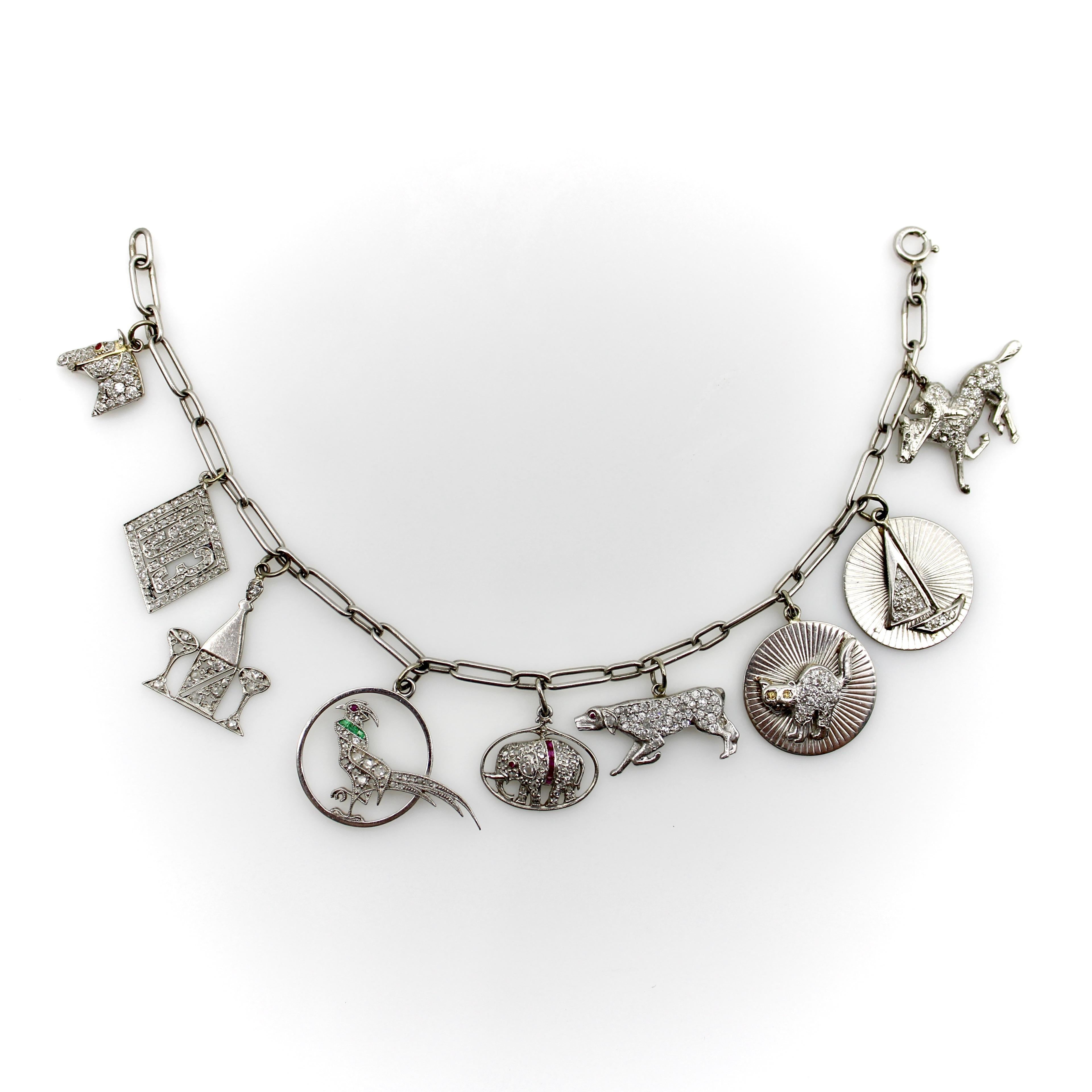Dieses außergewöhnliche Armband aus Platin stammt aus der edwardianischen Ära und hat noch alle originalen Charms, was es zu einem ganz besonderen Stück macht. Neun mit Diamanten besetzte Charms hängen an einer büroklammerähnlichen Kette - jeder