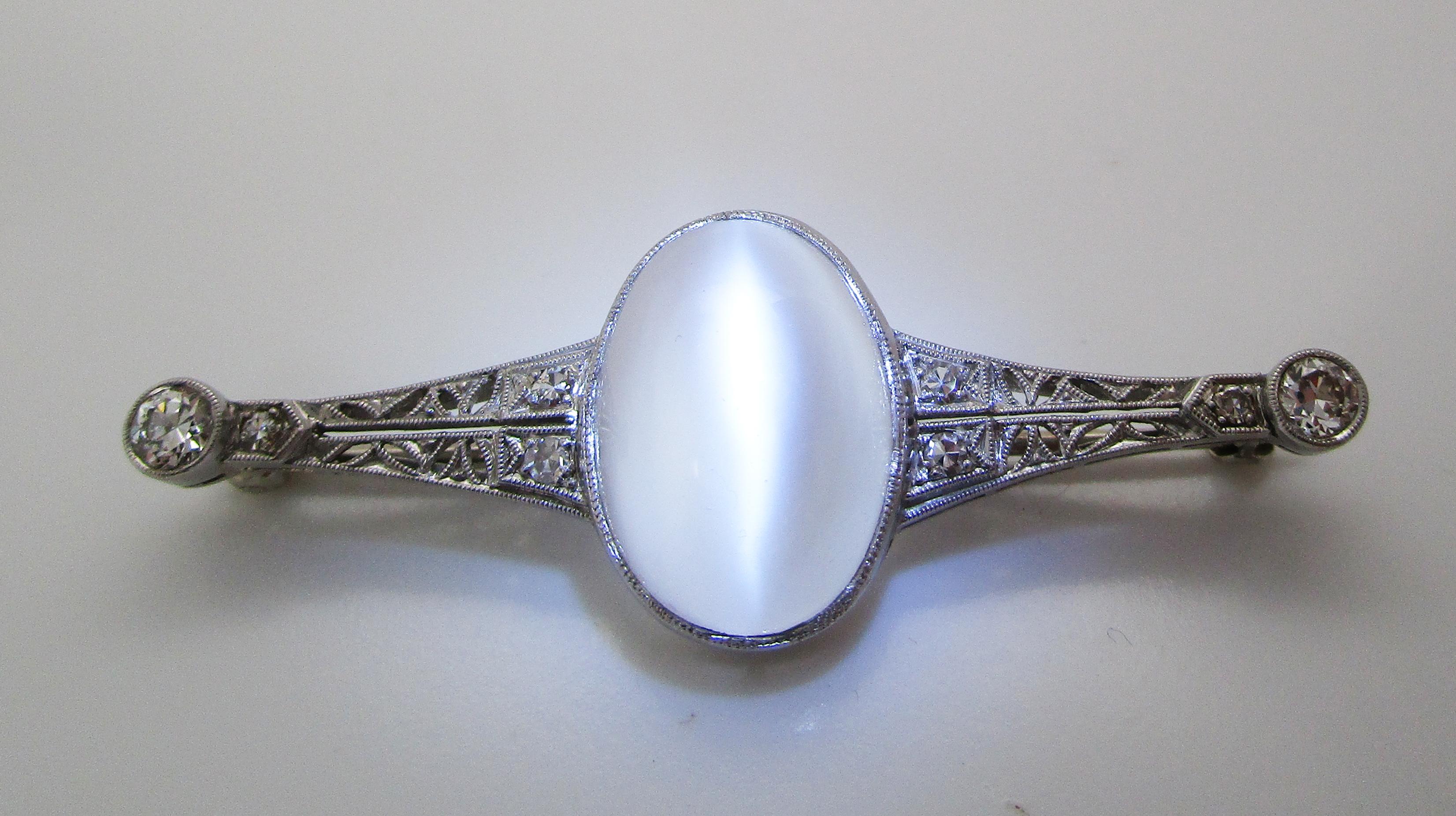 This beautiful Edwardian pin is in platinum with gorgeous pierced filigree set with stunning diamonds and an enchanting cat’s eye moonstone center! The pin has a lovely bar pin layout with a diamond at each end and a gorgeous moonstone center. The