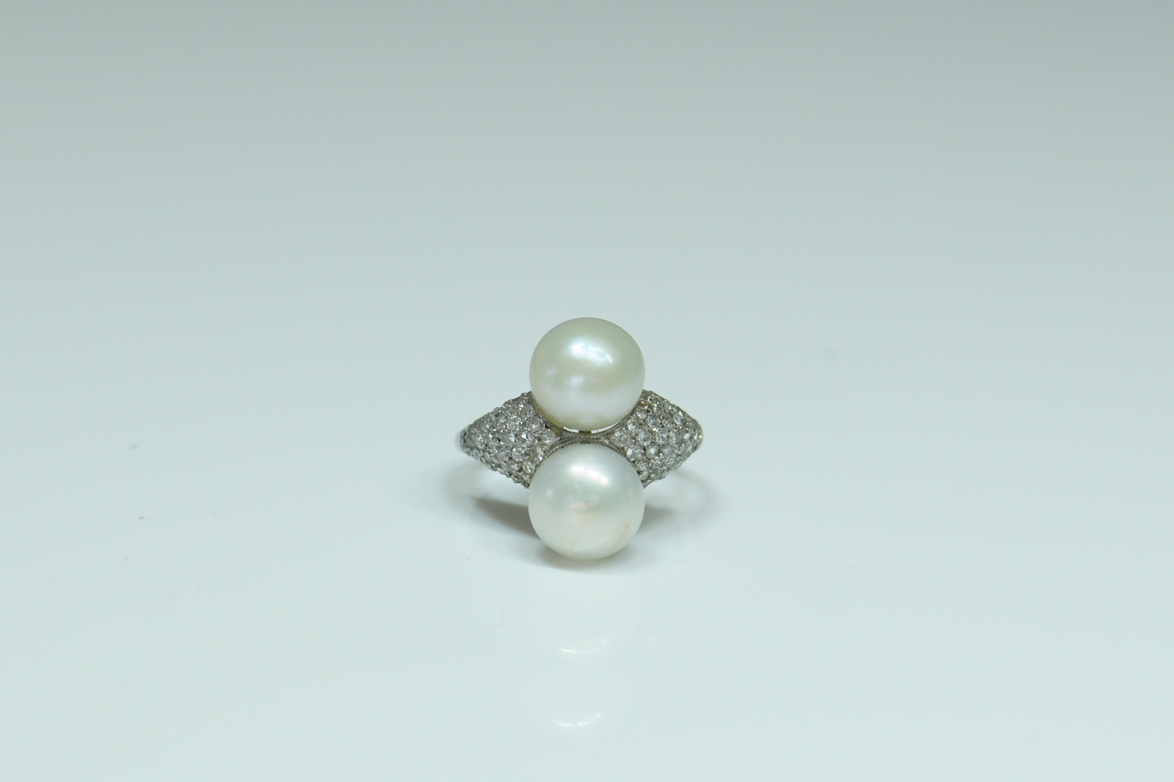 A lovely platinum ring that was made circa 1900-1910. It has been set with two natural pearls in the middle and diamond set shoulders on both sides. The backside work of this pretty ring is as beautiful as the front. It would make a pretty dress