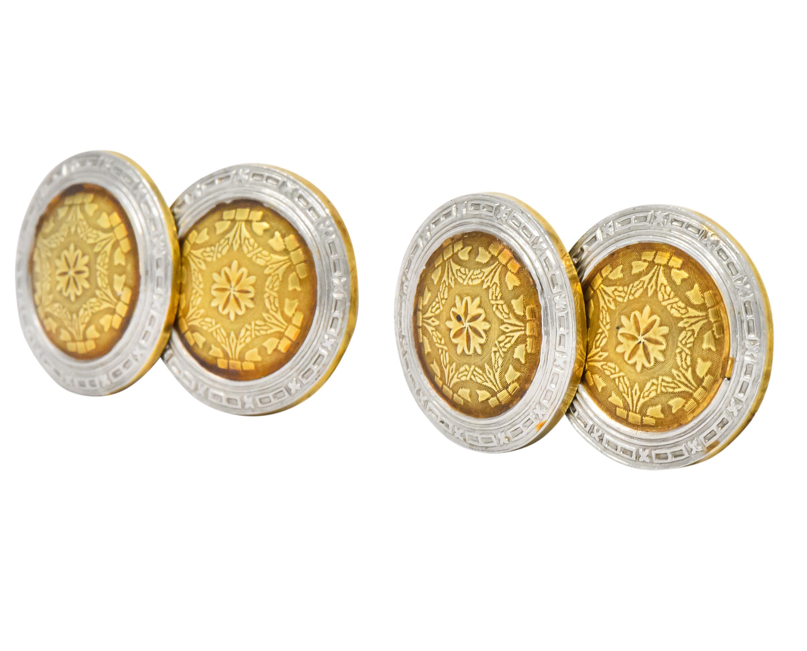 Link style cufflinks with matching discs on each end measuring 15.3 mm

Discs feature a platinum-topped outer circle with an engraved X and dash pattern and a central gold circle with engraved bow and foliate motif centering a floral design

Circa