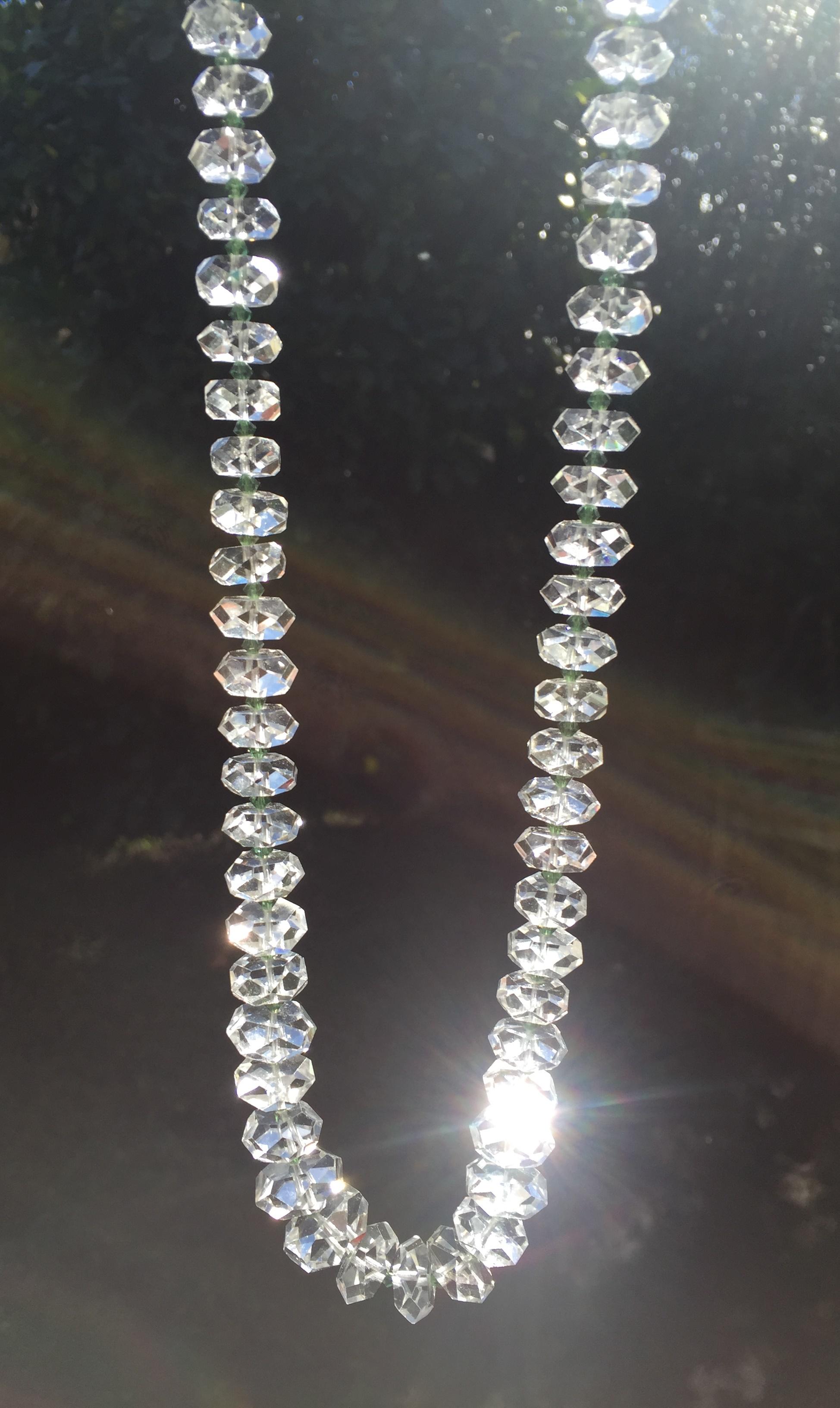 Offered here is a massive Edwardian genuine rock crystal necklace in a classic opera length, Circa 1910. It consists of a continuous strand of perfectly graduated discs of hand-faceted rock crystal; between each of the discs is a tiny bicone emerald