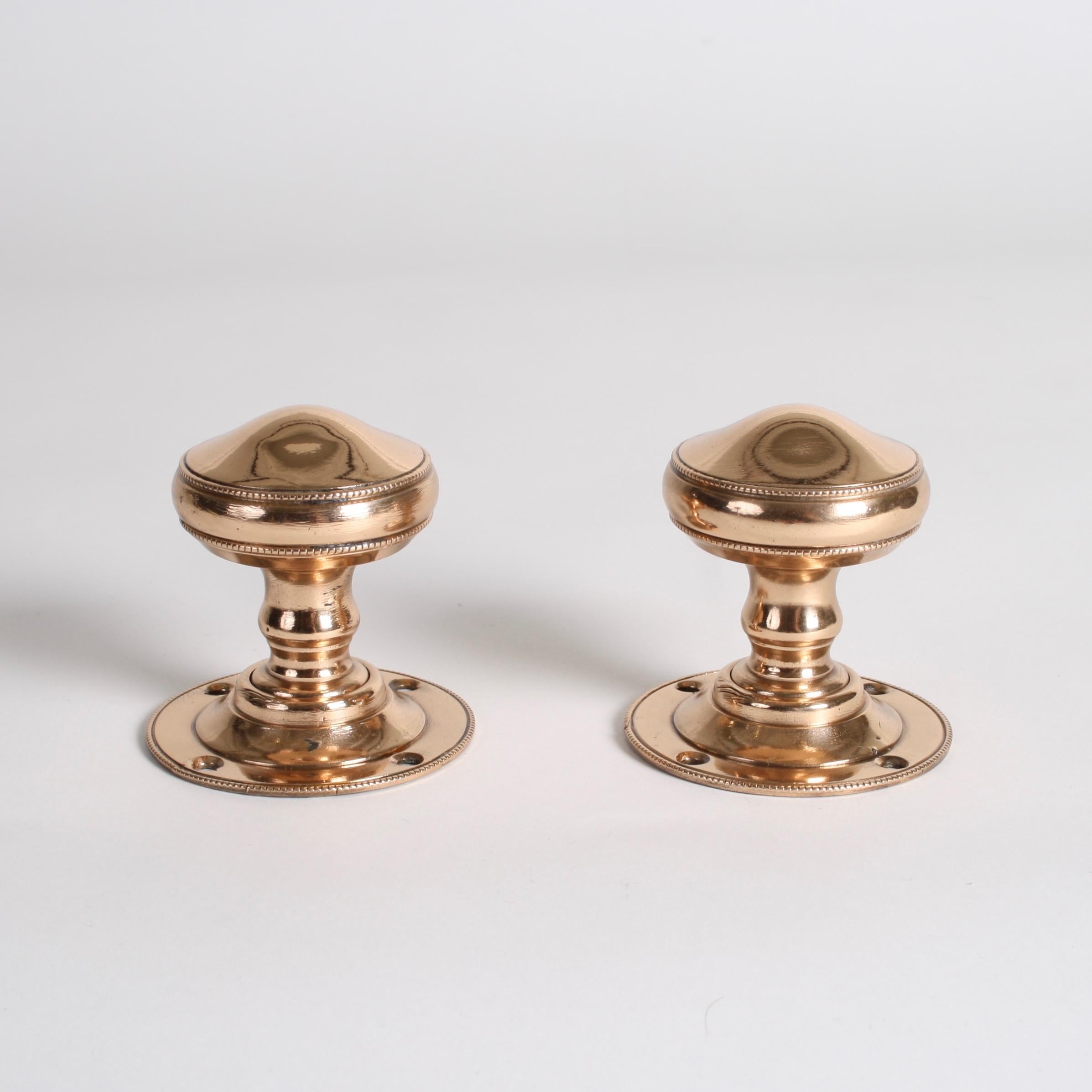 A pair of Edwardian rose brass door knobs with piping to outer edges.