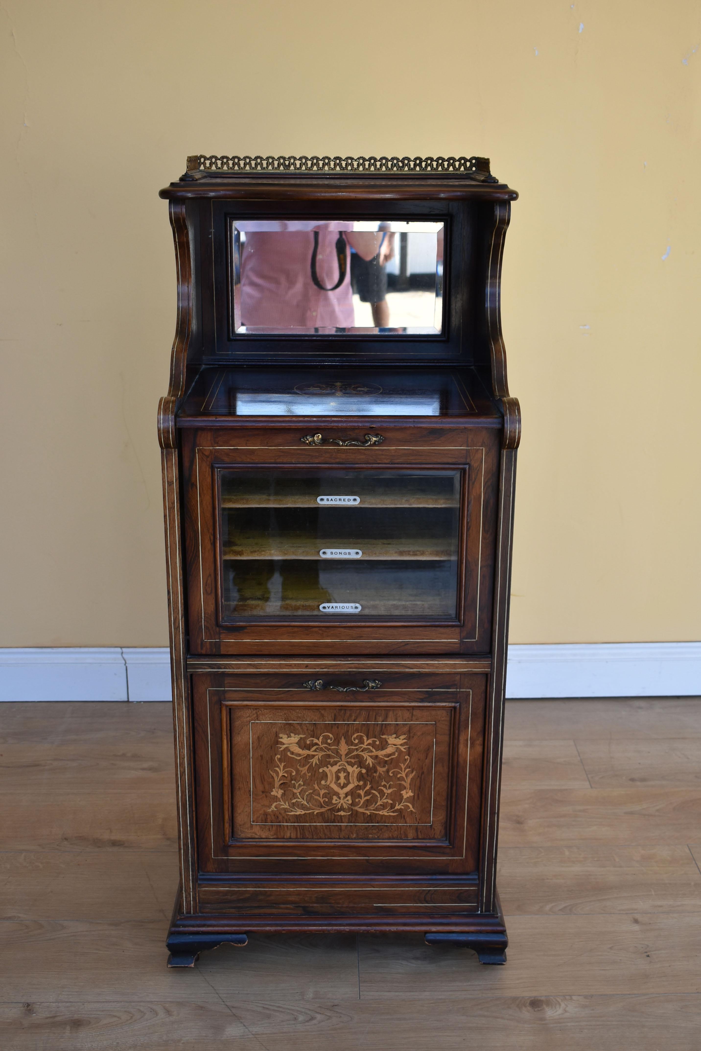 For sale is a good quality Edwardian rosewood and boxwood line inlaid music cabinet, with a brass gallery and mirror back, having a glazed fall front below, enclosing fabric lined shelves, labelled, sacred, song, various. Below this is a further
