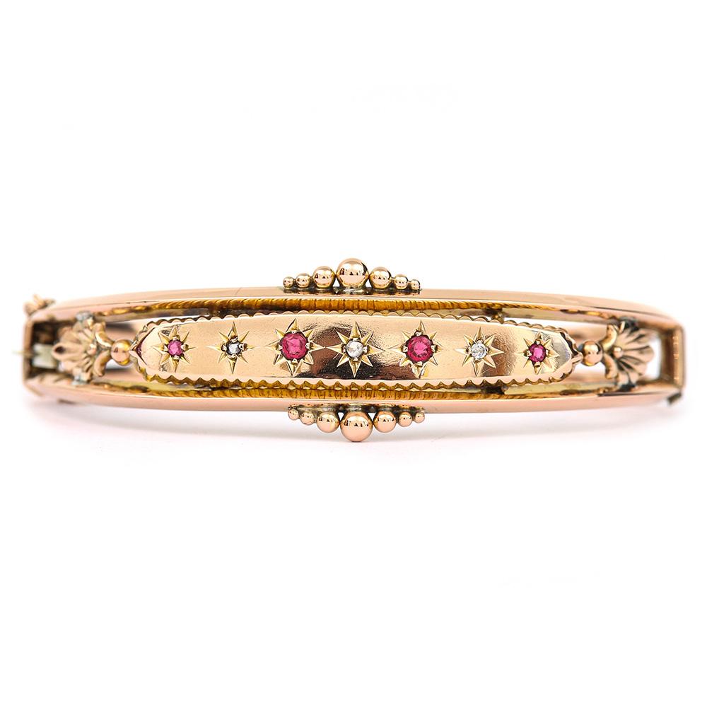 An attractive 9 karat gold Edwardian ruby and diamond bangle. It is in lovely condition with four facet cut rubies and three small mixed cut diamonds that are star set in the oval central panel. This antique hinged bangle has bead decorated border