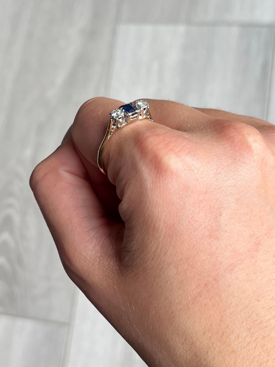 This classic three stone ring holds an emerald cut sapphire measuring 15pts at the centre and ether side there is a shimmering round cut diamonds measuring 15pts each. Modelled in 18ct gold.

Ring Size: T or 9 1/2 