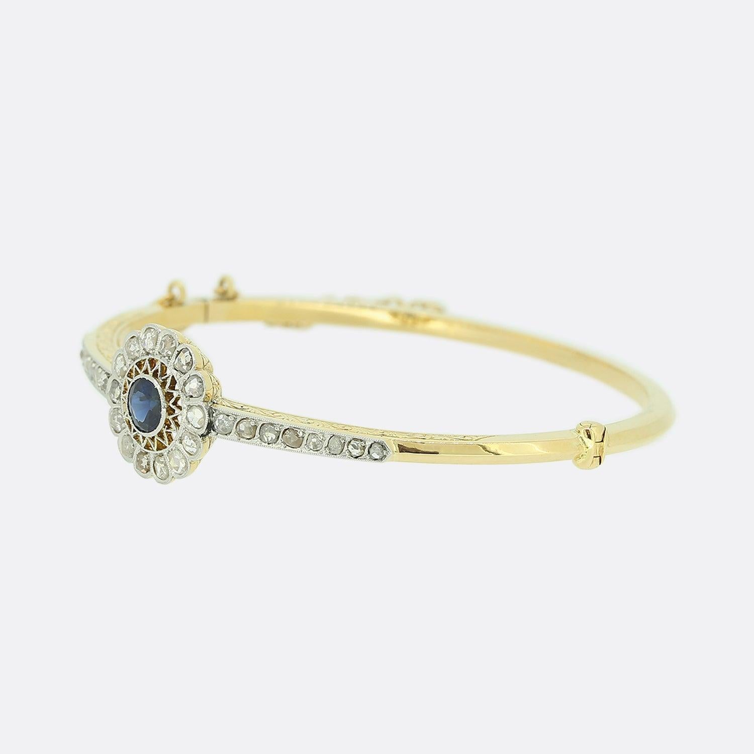 This is a beautiful 18ct yellow gold bangle from the Edwardian era. The bangle features a central sapphire surrounded by a border of rose cut diamonds and a further 8 diamonds on each shoulder. The dark blue of the sapphire is highly complimented by