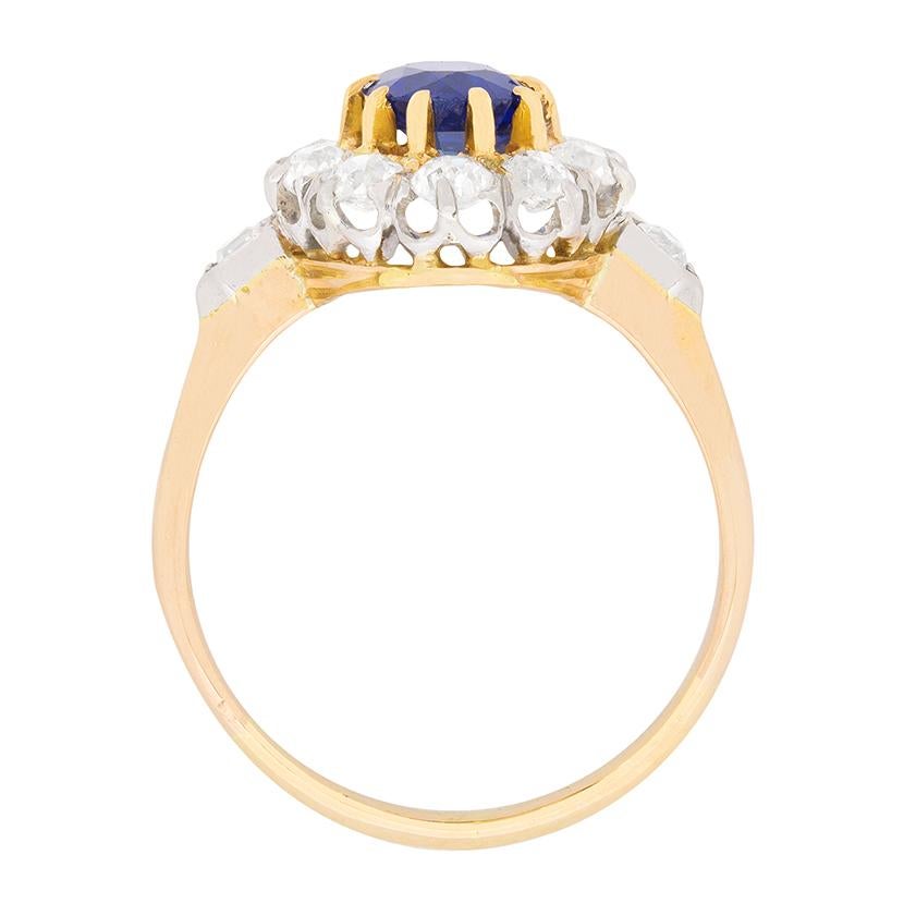 In the centre of this beautiful ring is a cornflower blue sapphire weighing 1.23 carat. It is a natural stone and is claw set using 18 carat yellow gold. The halo of diamonds, which are old cuts, has a total weight of 1.70 carat. There are ten