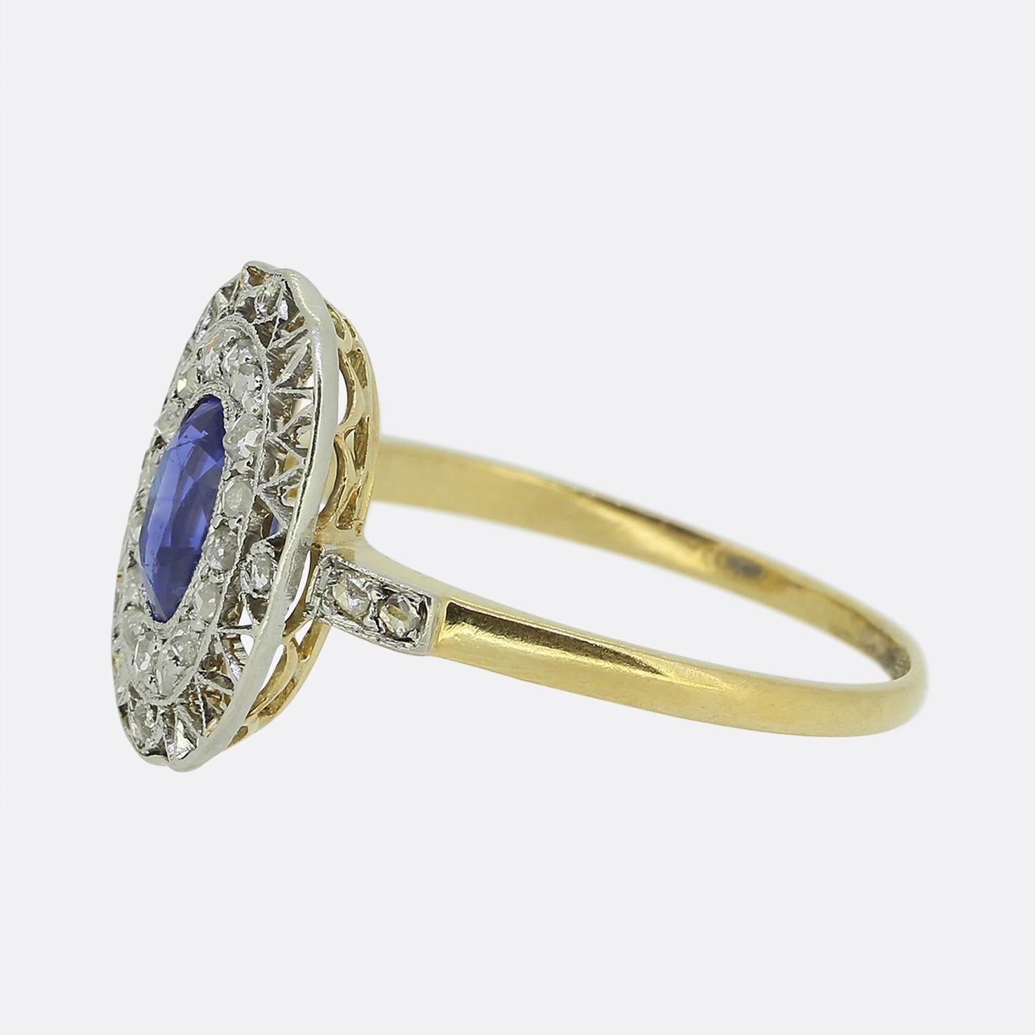 Here we have a delightful sapphire and diamond cluster ring dating back to the Edwardian period. This antique piece showcases a single oval faceted sapphire at the centre of the face. This principal stone possesses a wondrous cornflower blue colour