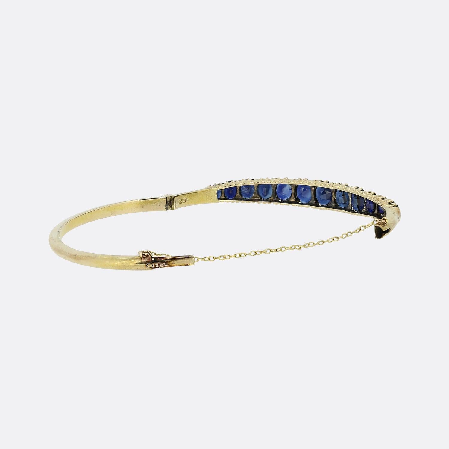This is a beautiful 18ct yellow gold Edwardian sapphire bangle. The bangle features thirteen cushion cut blue sapphires that graduate towards the centre and have been set in an 18ct yellow gold setting with a secure push down clasp and safety