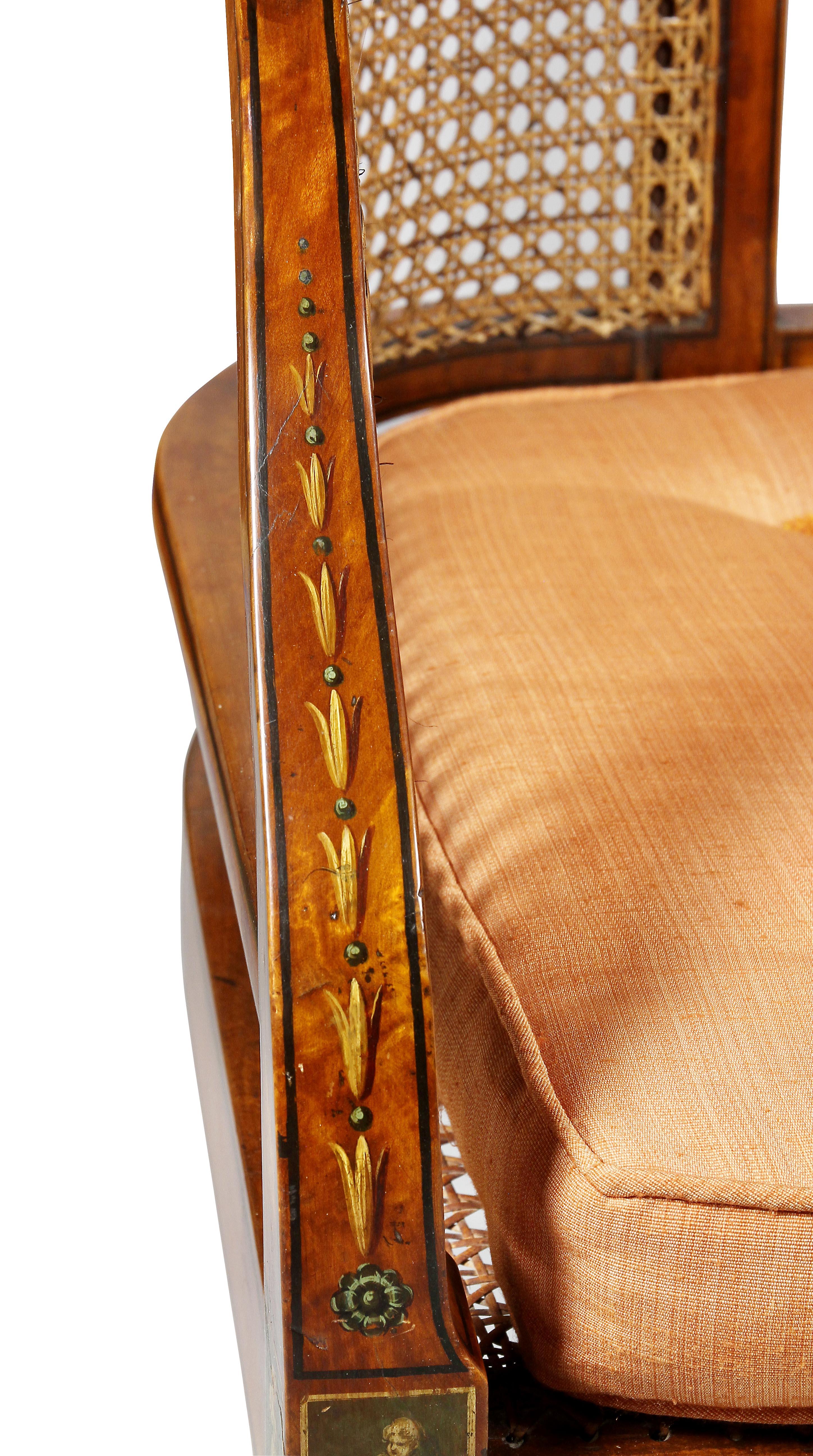 With a newly caned arched back with painted medallions over a caned seat with loose cushion, raised on square tapered legs and spade feet.