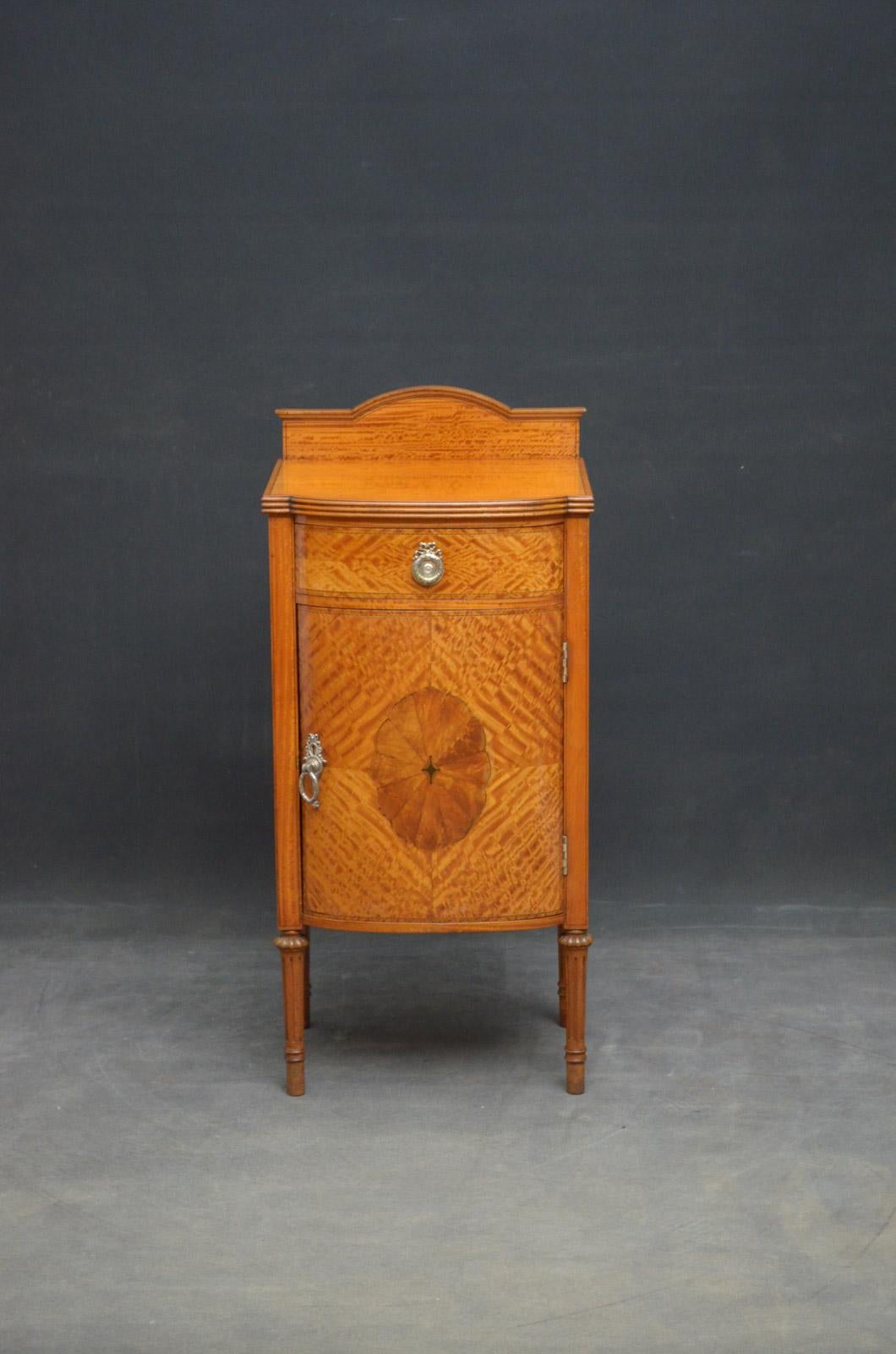 Sn4651, fine quality Edwardian satinwood bedside cupboard of bowfronted design, having shaped upstand and string inlaid top with reeded edge above a frieze drawer and cupboard door, all fitted with original bras handles, all standing on turned,
