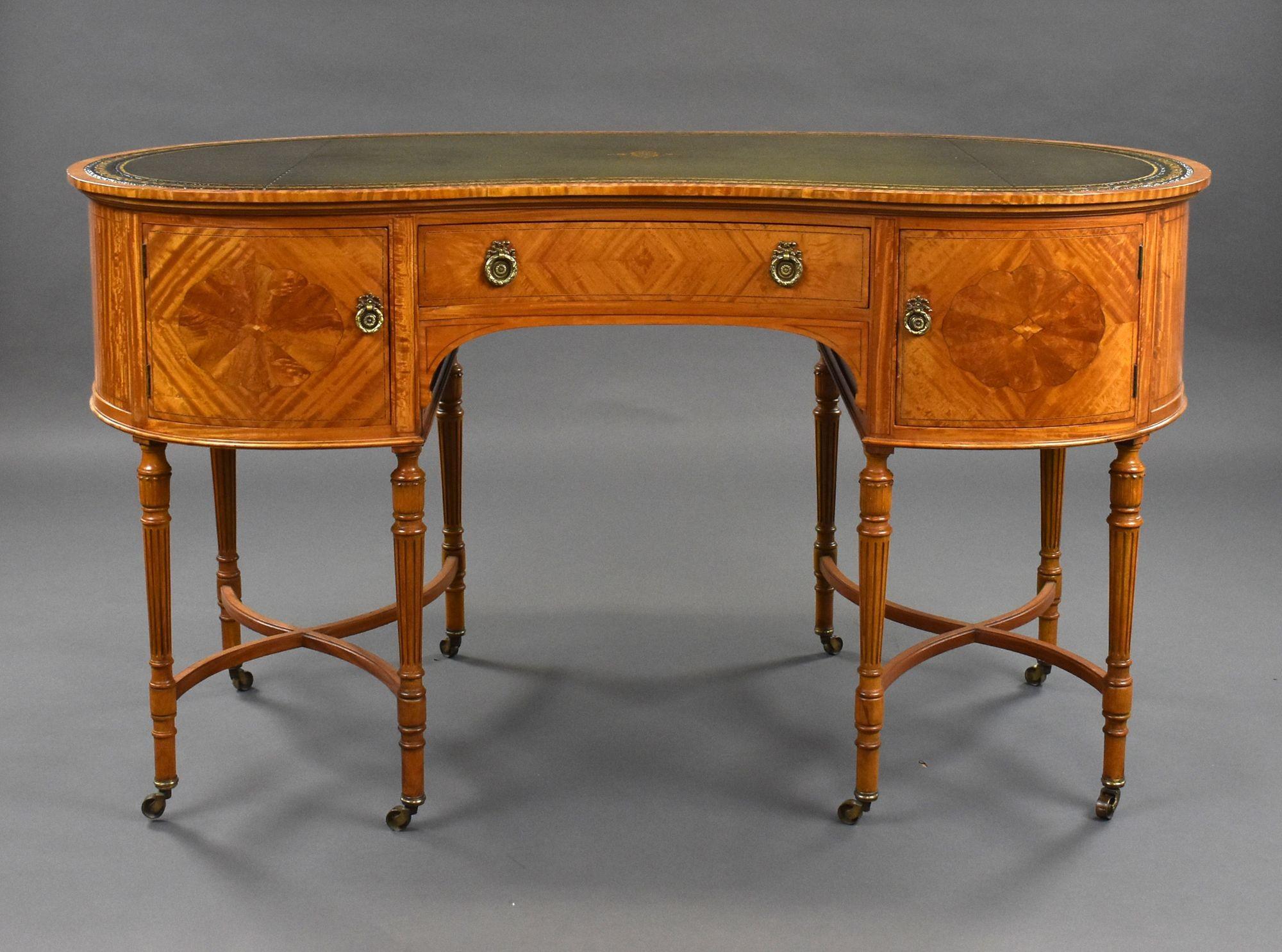 For sale is a good quality Edwardian satinwood kidney shaped desk, having a quality green leather writing surface, decorated with gold tooling and a centre motif, above a single drawer to the centre flanked by a cupboard on either side. Standing on