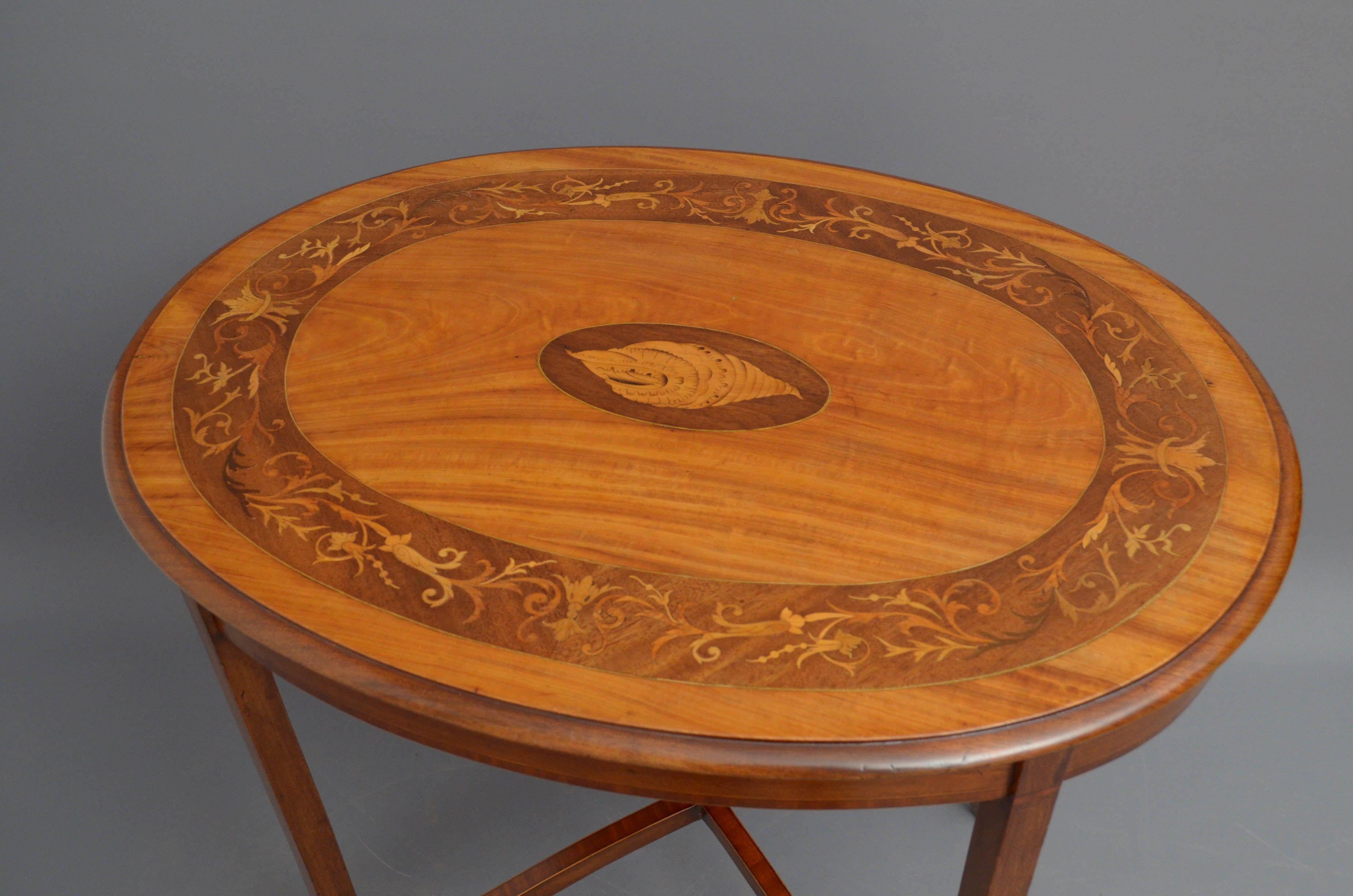 Sn5198 Edwardian satinwood lamp table of oval design, having neo classical inlaid to the top with conch shell inlaid centre above crossbanded frieze, standing on slender legs united by shaped and crossbanded stretchers. This antique table retains