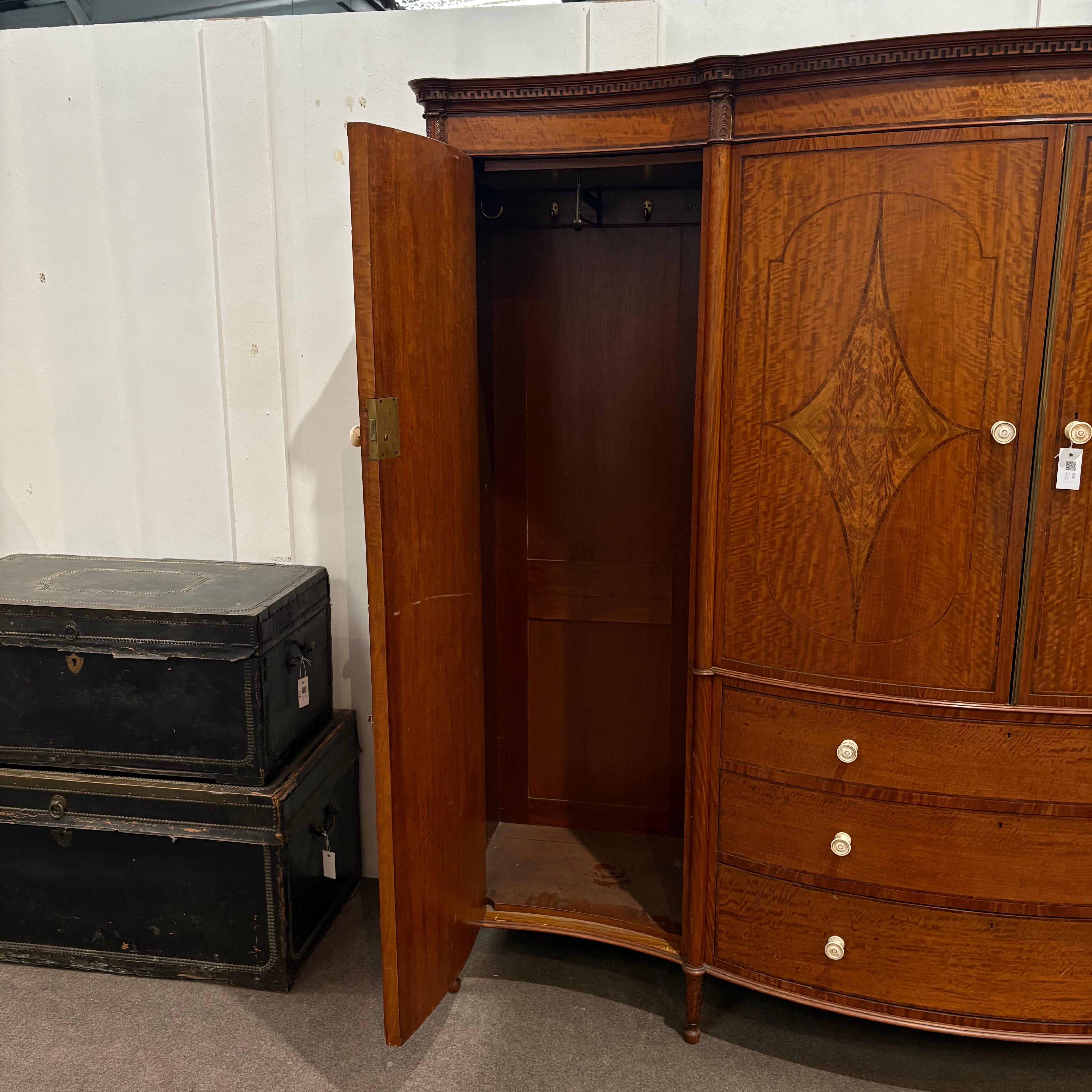 EIN EDWARDIANISCHER SATINIERTER UND MIT QUERBÄNDERN VERSEHENER SERPENTINE-SCHRANK AUS DEM FRÜHEN 20.
mit zwei seitlichen Schranktüren, in der Mitte vier verschiebbare Einlegeböden, darüber drei abgestufte lange Schubladen, mit gedrechselten