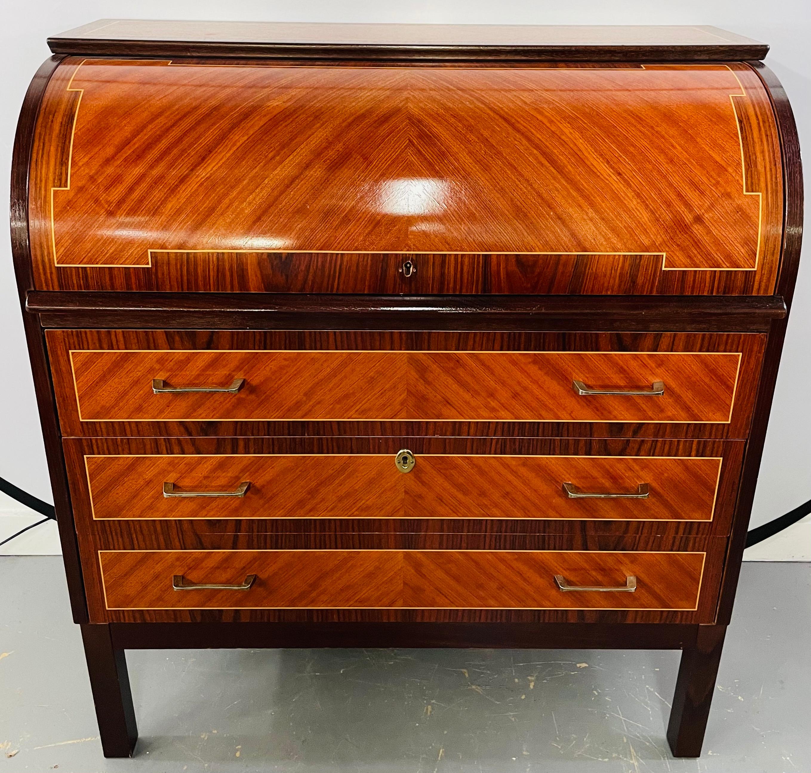 An Edwardian Sheraton revival style flame mahogany cylinder desk or commode. The cylinder opening reveals fitted interior with three small drawers having marquetry inlaid floral decoration. The desk / commode features three drawers seating on