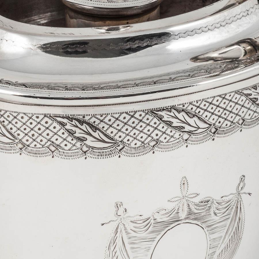 As a pot designed to keep gravy warm, this antique silver argyle (argyll) is a reproduction of a style made in the late 18th century during the reign of King George III. The oval vase-shaped body is beautifully hand engraved with a band of leaf and