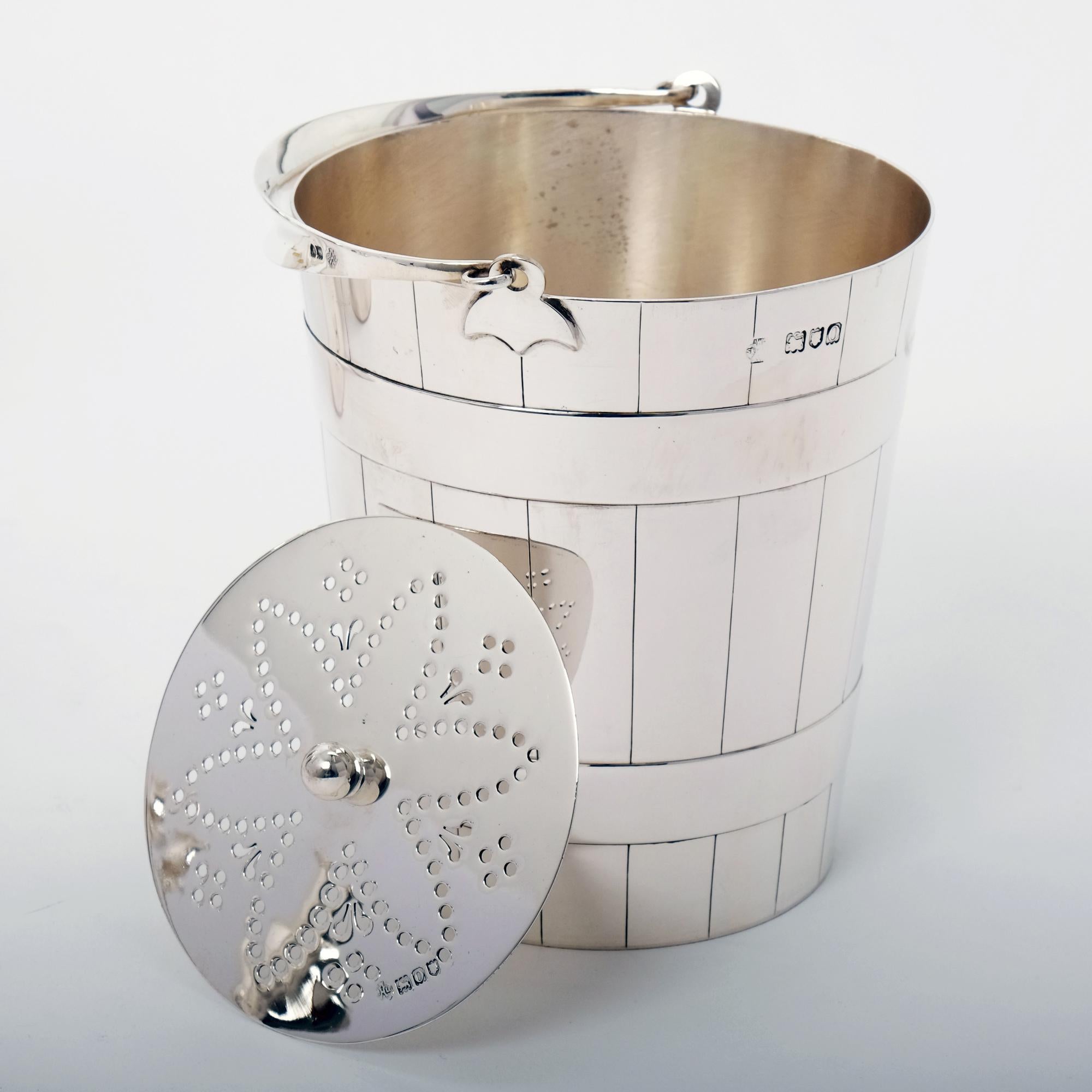 An unusual and very stylish silver ice bucket with engraved and applied bands to give the appearance of a traditional wooden pail. The ice bucket has a separate pierced draining plate inside and swing handle, both with a London hallmark for William