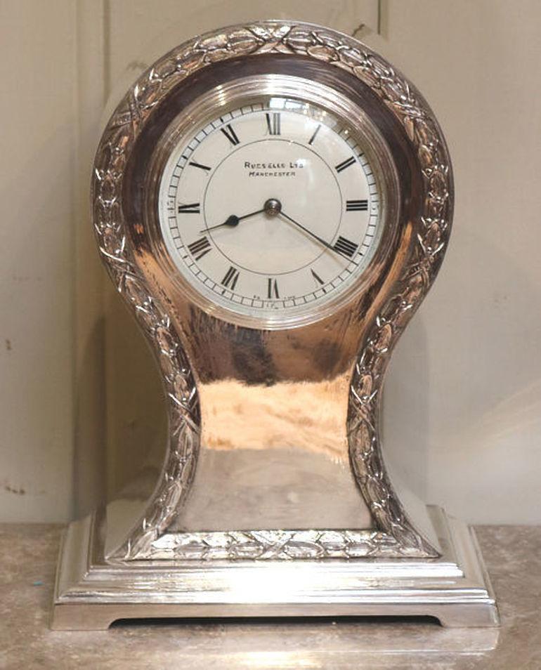 A heavy, well made silver plated balloon clock dating to the early 20th century. It has a waisted case with wheatsheaf edging and an ogee moulded base. The white enamel dial has a bevel edge convex glass and is signed by the original retailers