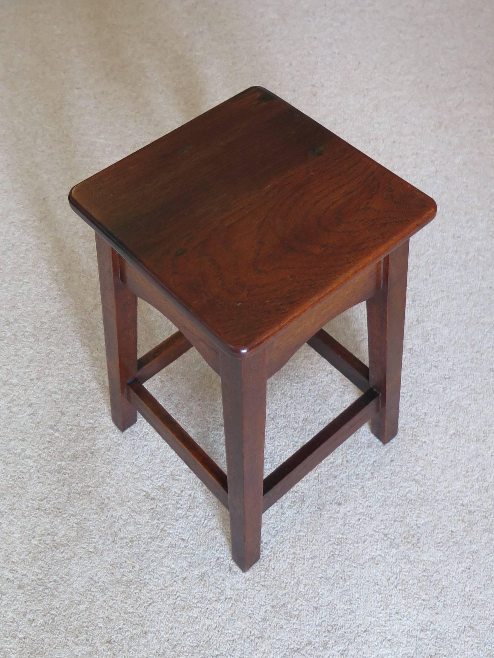 This is a handmade Edwardian solid oak stool with an elm top, which could be used as a stand or a side table.

The top is square with rounded edges and is supported on four square tapered legs with a deep shaped frieze beneath the top. Four lower