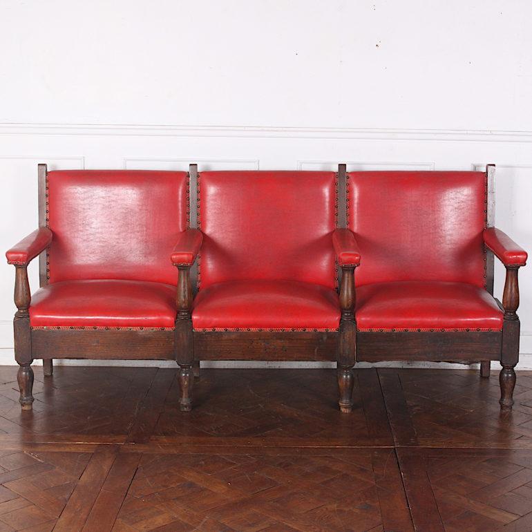 Large oak-framed three-seat red faux-leather bench with baluster-turned legs and arm supports, circa 1910.



  