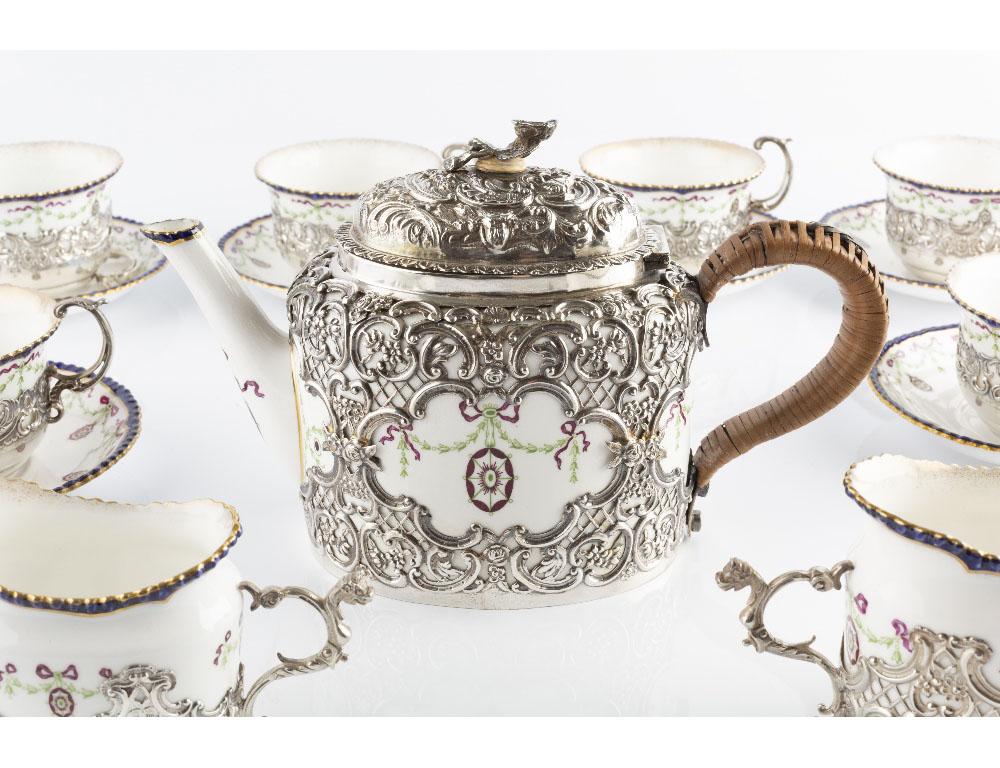 An Edwardian sterling silver mounted Royal Worcester tea service, the porcelain decorated in green and puce with ribbon tied swags and medallions, the silver mounts intricately pierced and embossed with flowers, 'C' scrolls and trellis work, by