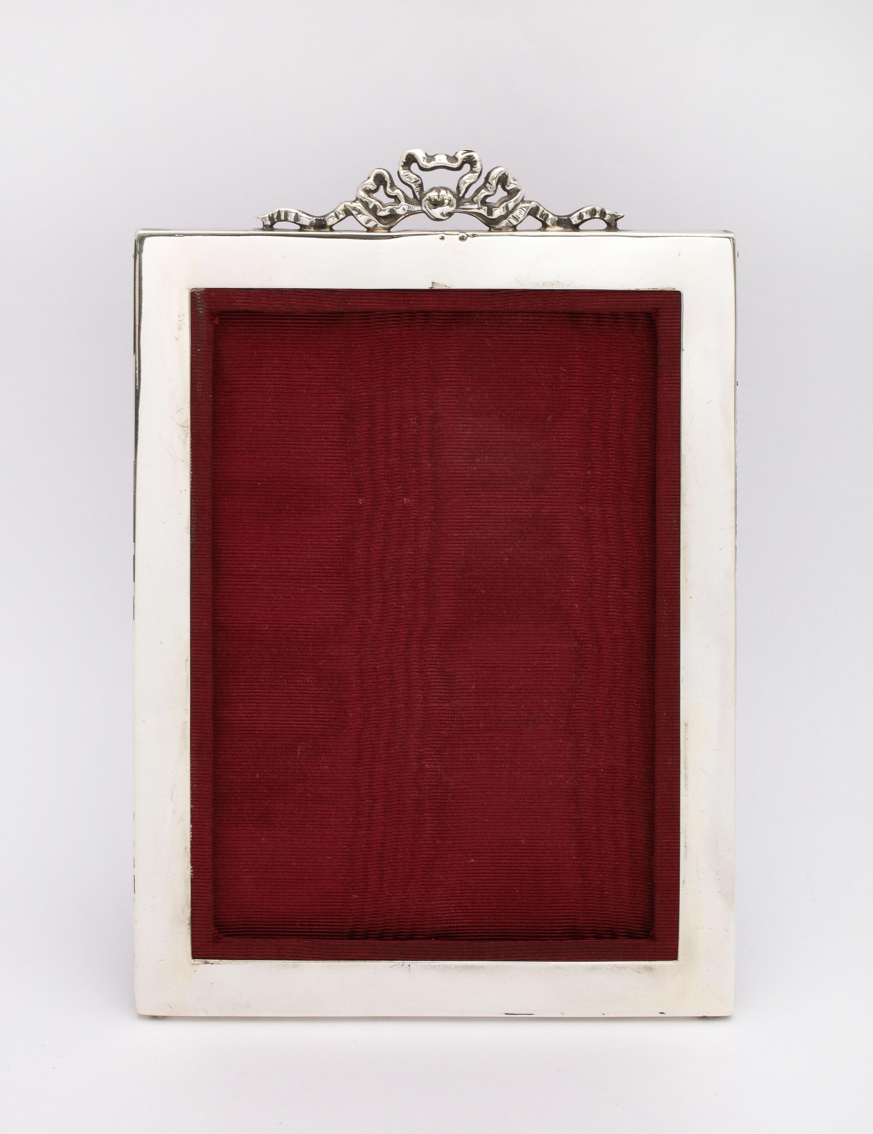 Edwardian, sterling silver picture frame (having a bow finial), Birmingham, England, year-hallmarked for 1901, E. Mander and Son, Ltd. - makers. Frame is backed in burgundy moire. Frame measures 7 inches high (at highest point) x 5 inches wide x 4