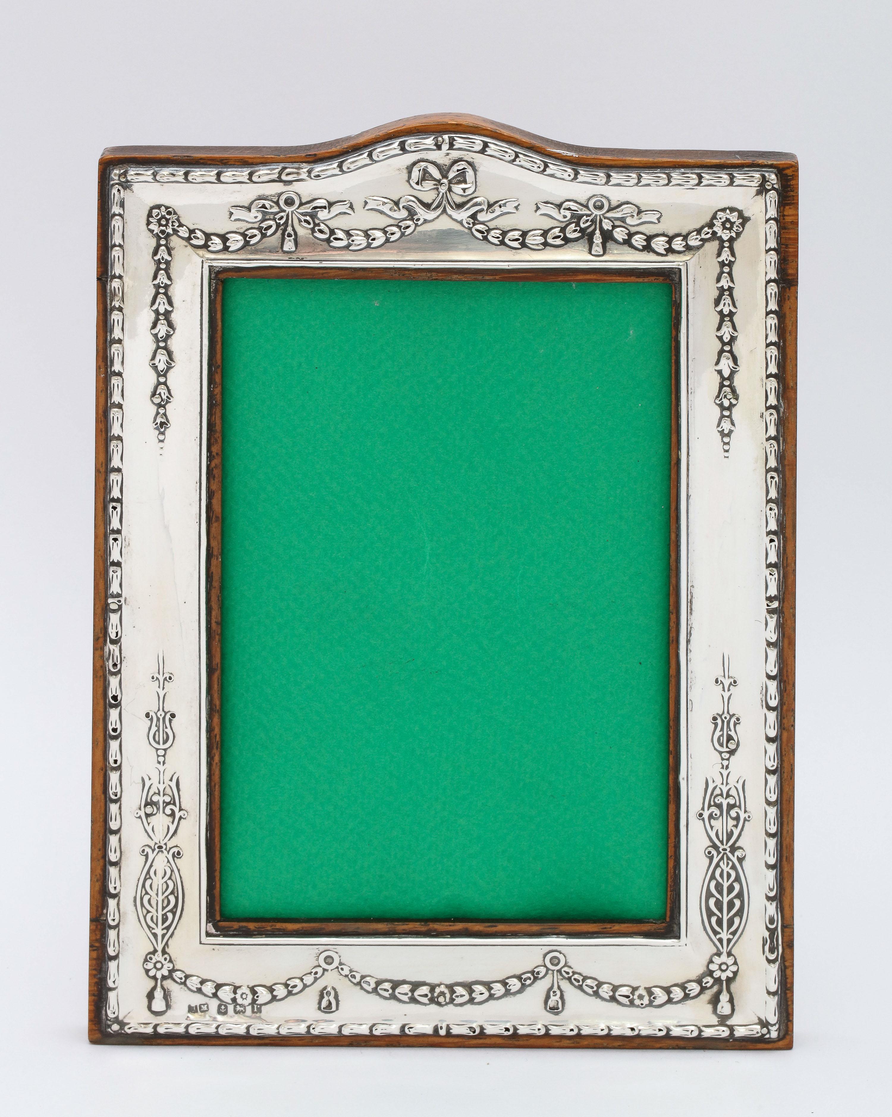 Edwardian, sterling silver, wood-backed picture frame, Birmingham, England, year-hallmarked for 1916, H. Matthews - maker. Decorated with garlands and bows. Measures 7 3/4 inches high (at highest point) x 5 3/4 inches wide (at widest point) x 5