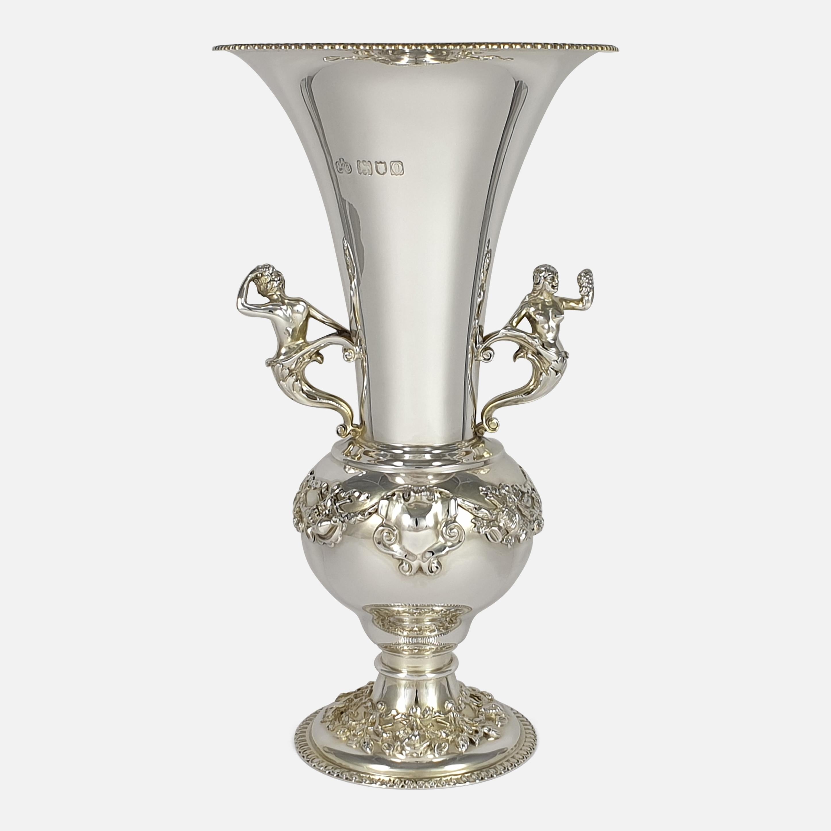 An Edwardian sterling silver vase by Elkington & Co. Ltd, London, 1909. The bulbous body is raised on a pedestal base that leads to a flared neck. The vase is decorated with vacant cartouches, musical instruments and scrolls, and is completed with a