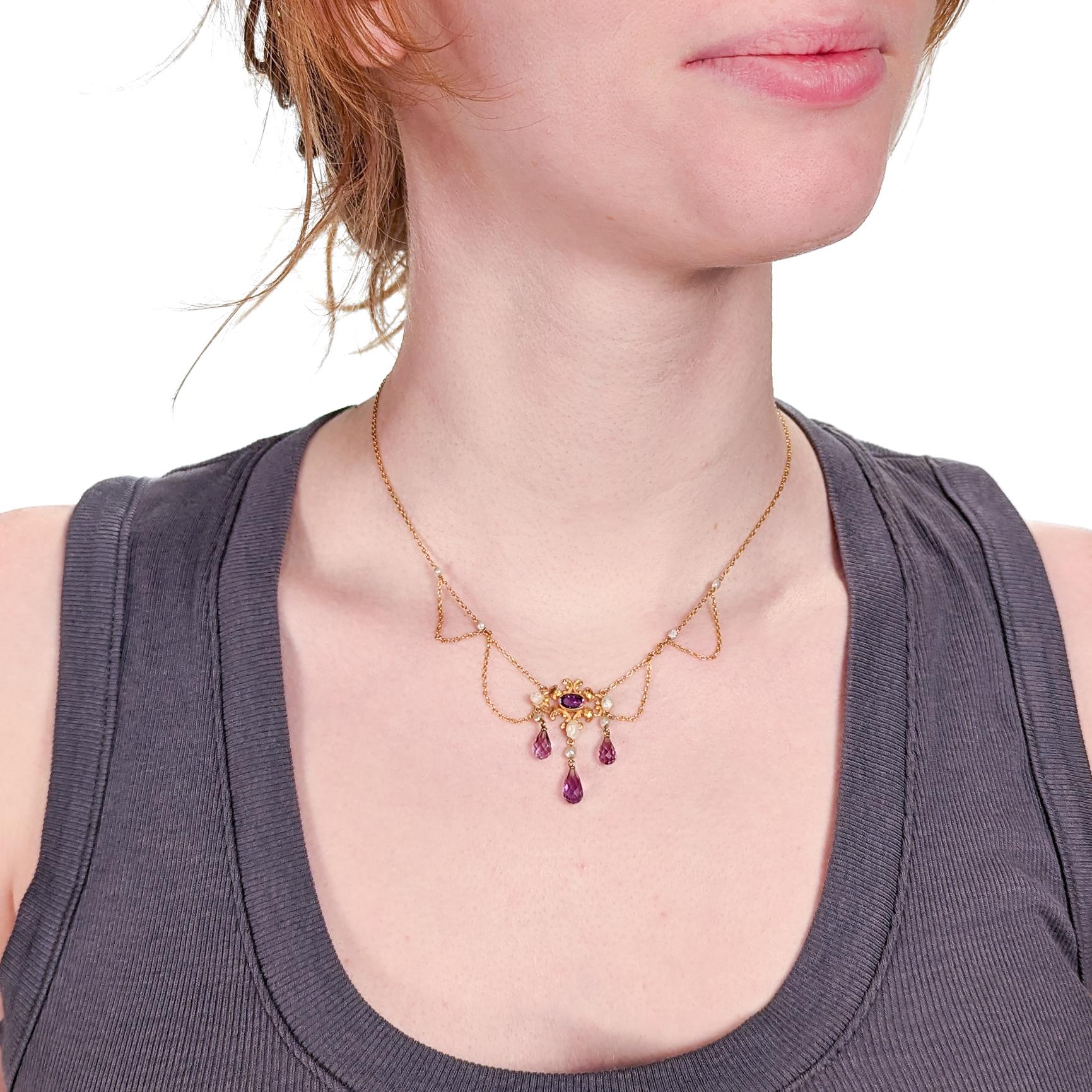 A fine Edwardian style festoon necklace.

In 14 karat yellow gold.

Centered on an ornate gold yolk with a bezel-set oval-cut amethyst. 

Supporting 3 drops with freshwater river pearls and briolette-cut amethysts and flanked by several festooned