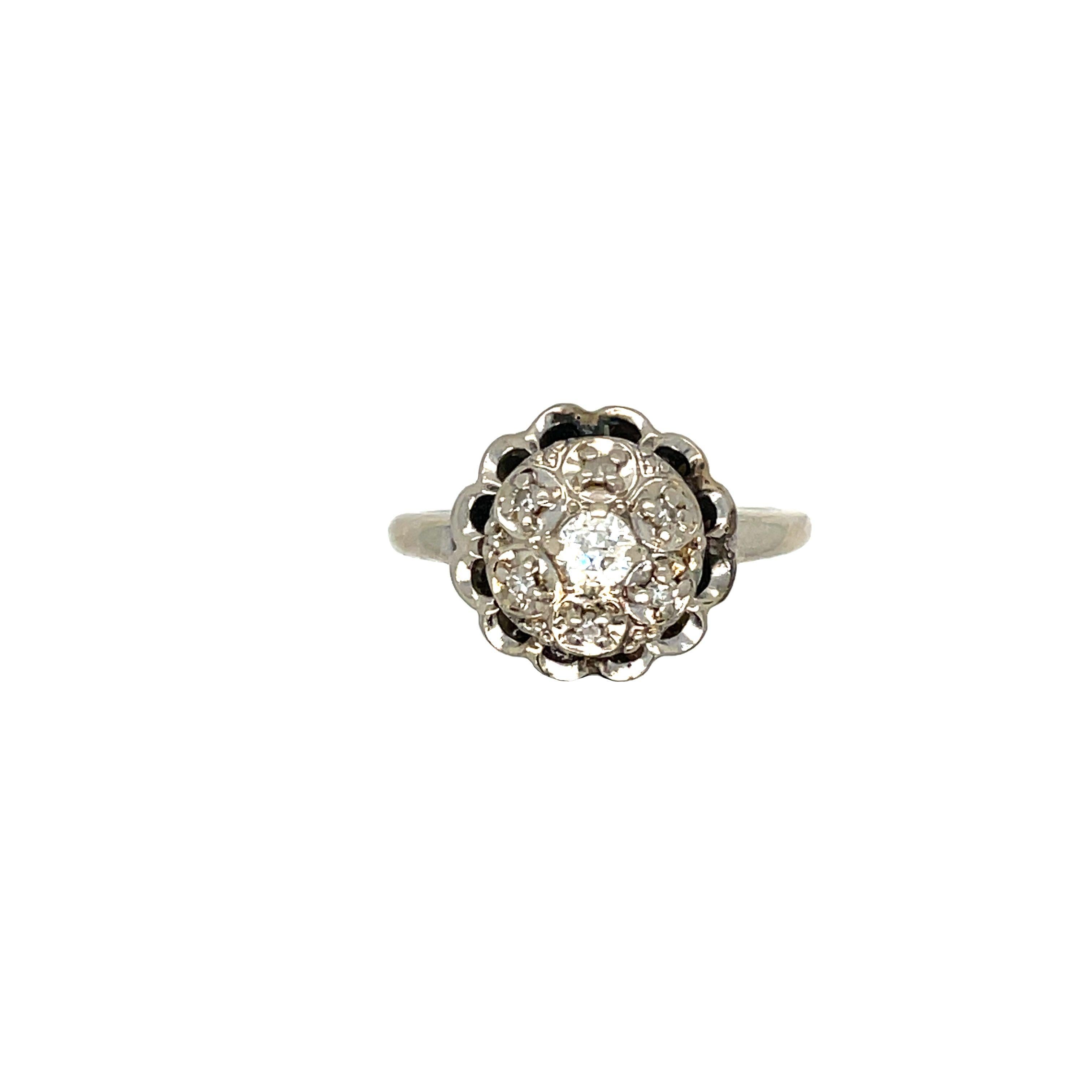 A show-stopping antique 14K white gold diamond cluster ring. 
The piece features 7 old European cut diamonds, which in total weight 0.20 carat with G-H color and VS2 clarity. This vintage beauty features a captivating centerpiece: a sparkling old