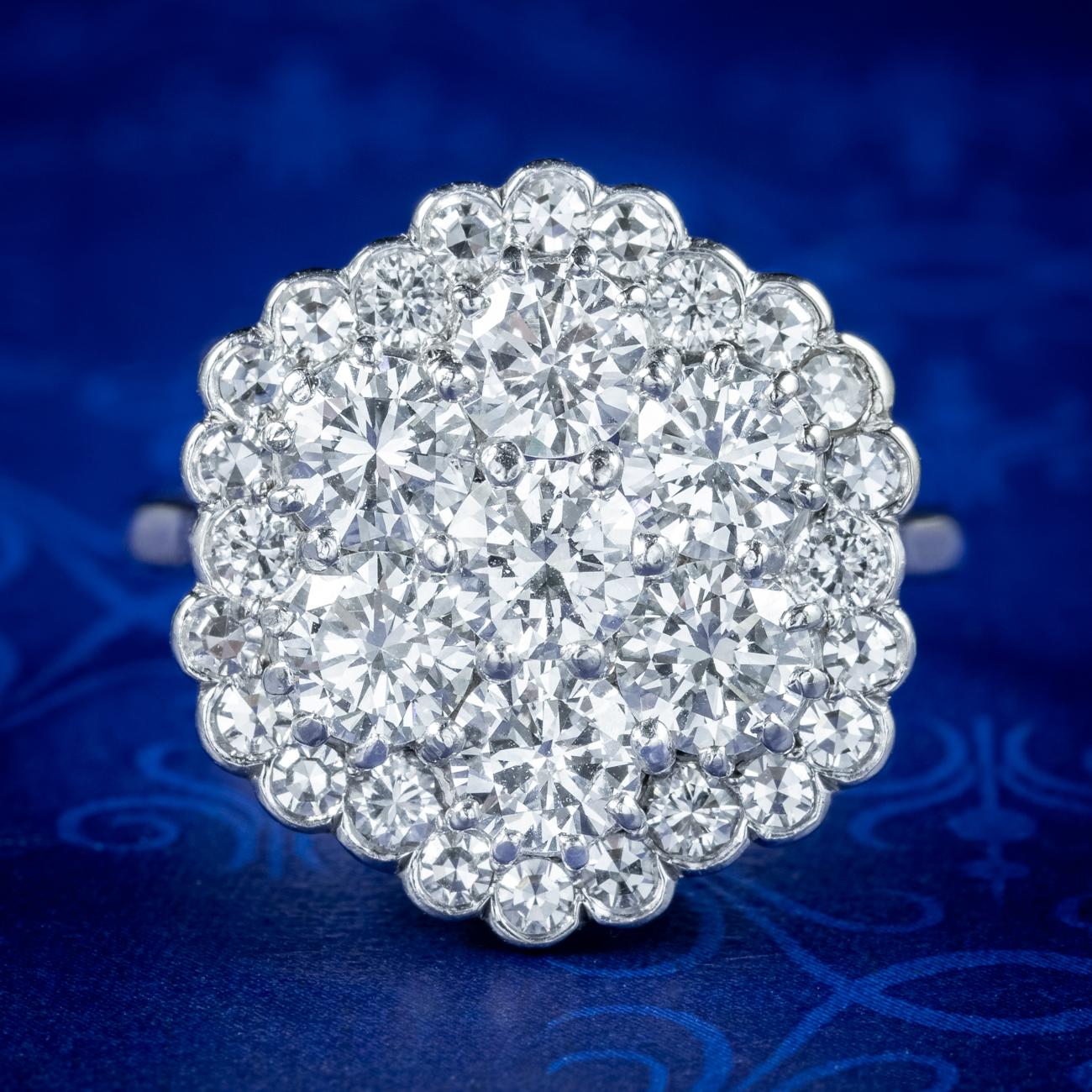 A glorious diamond flower cluster ring showcasing seven stunning brilliant cut diamonds arranged in a tiered cluster in the centre with a border of smaller diamonds chasing around the outside. The diamonds are exceptionally bright and full of life