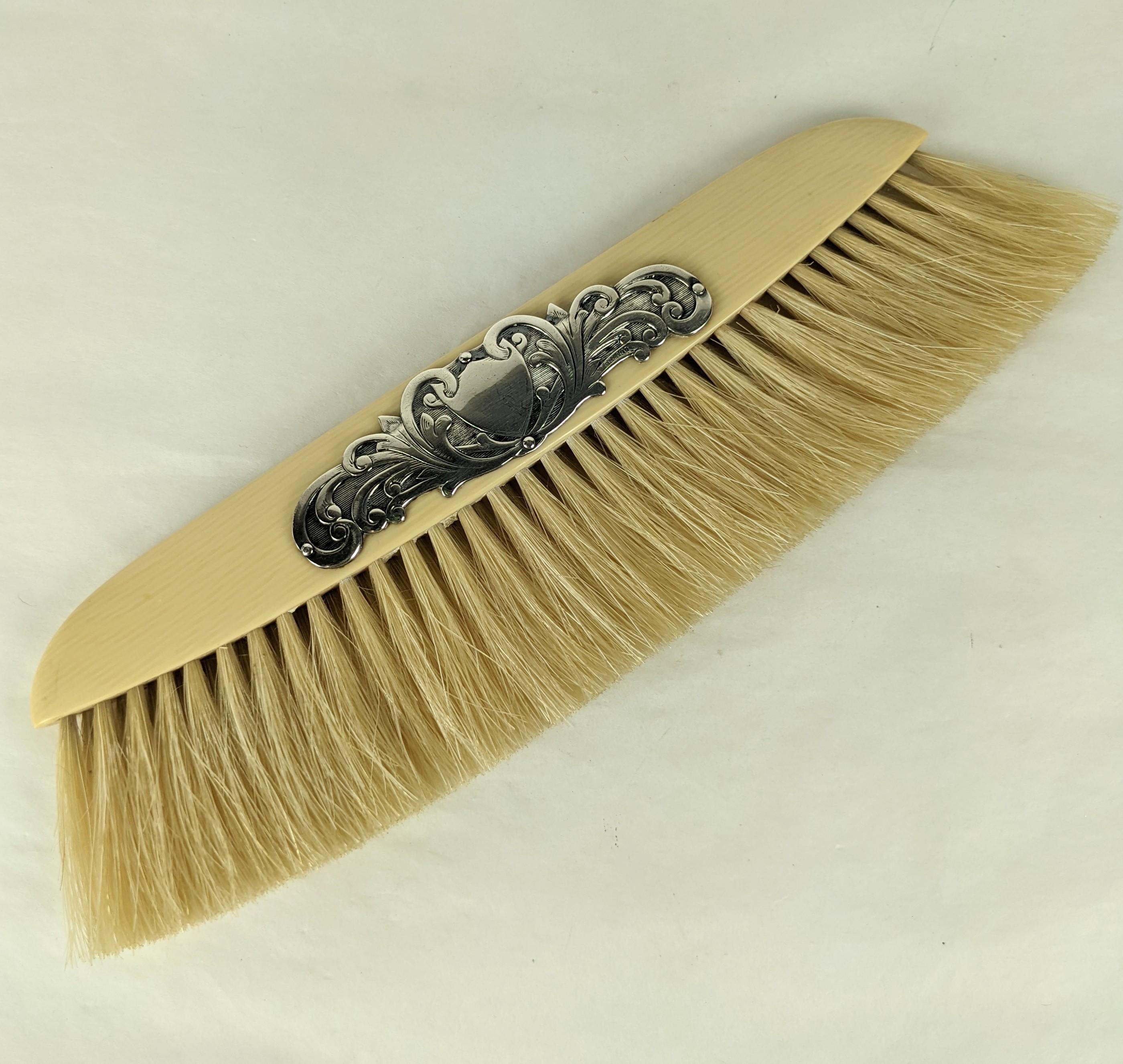 Edwardian table crumb brush from the early 20th century. Set with an elaborate central cartouche in sterling silver on a celluloid handle with natural bristles. 
Marked 