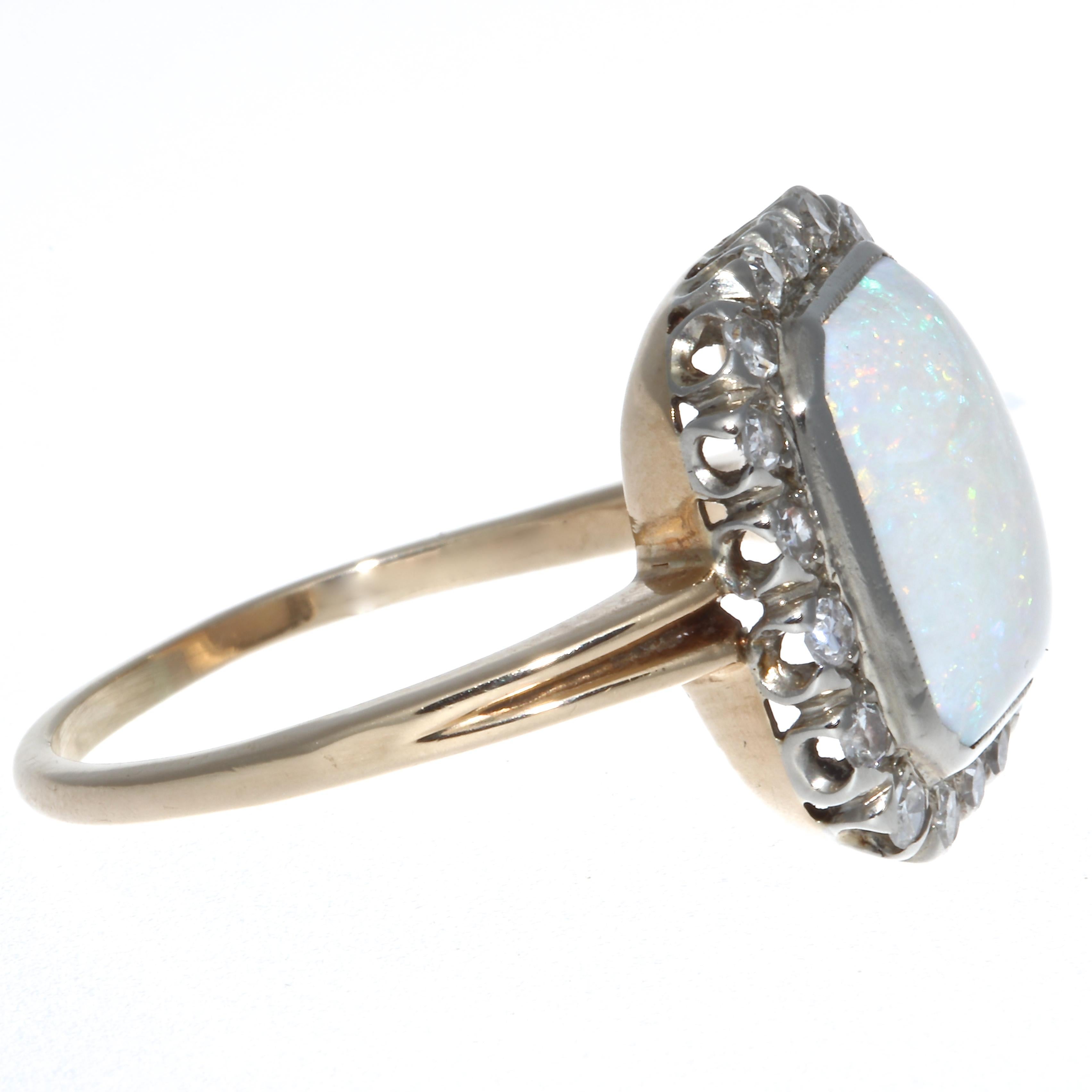 A rare antique Two-Tone opal ring. The beautifully shaped opal exhibits discreet colors throughout, maintaining it's regal presence while also exciting the eye. The opal is surrounded by 18 single cut diamonds, G,H color, SI clarity. The ring is 10k