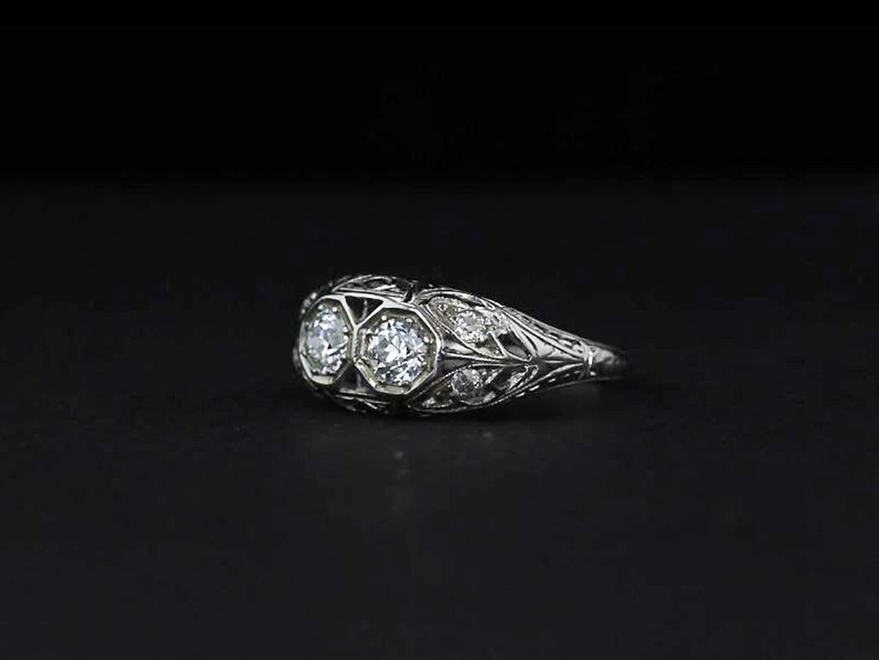 A toi-et-moi ring of the Edwardian era, this piece is handcrafted in 18k white gold and set with twin round diamonds in the center. Surrounding the larger stones is delicate open filigree work from which four additional diamonds sparkle.

The