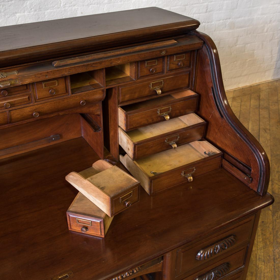 A fine quality solid walnut roll top desk with a fully fitted interior. Externally, the side and rear panels are al fielded (bevelled) and to the front the drawers have superb carved handles, below two brushing slides. The tambour opens and closes